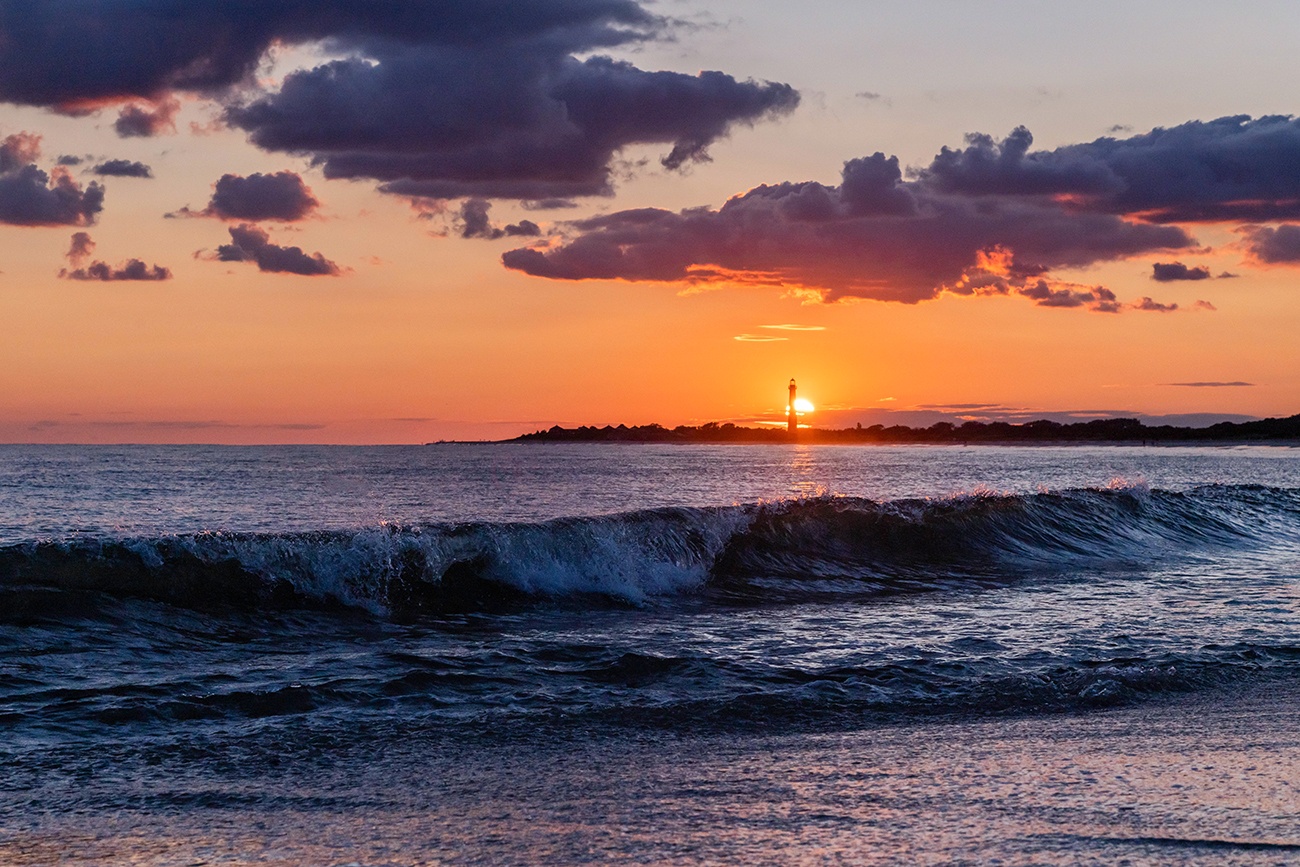 The sun setting directly behind the Cape May Lighthouse with a wave crashing