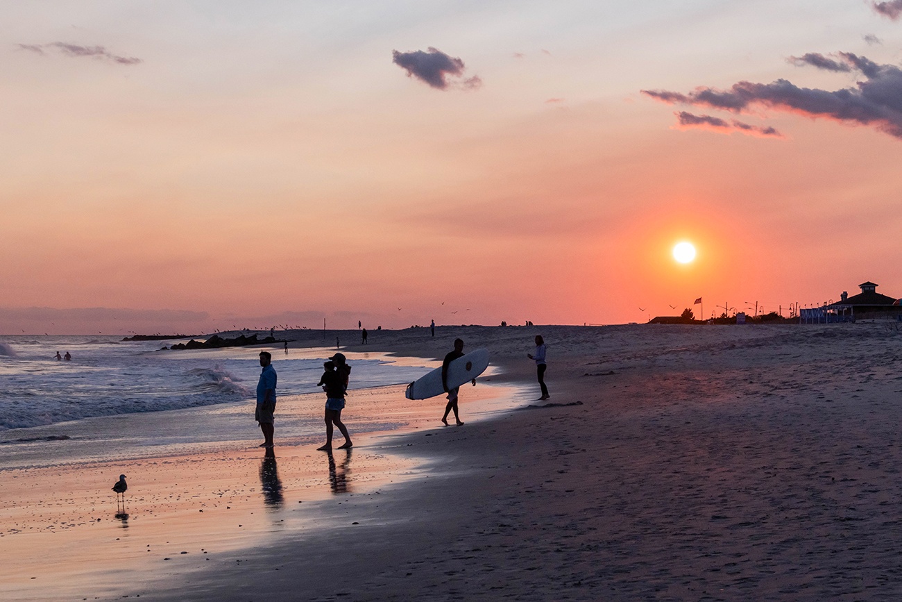 People and surfers by the ocean as the sun sets