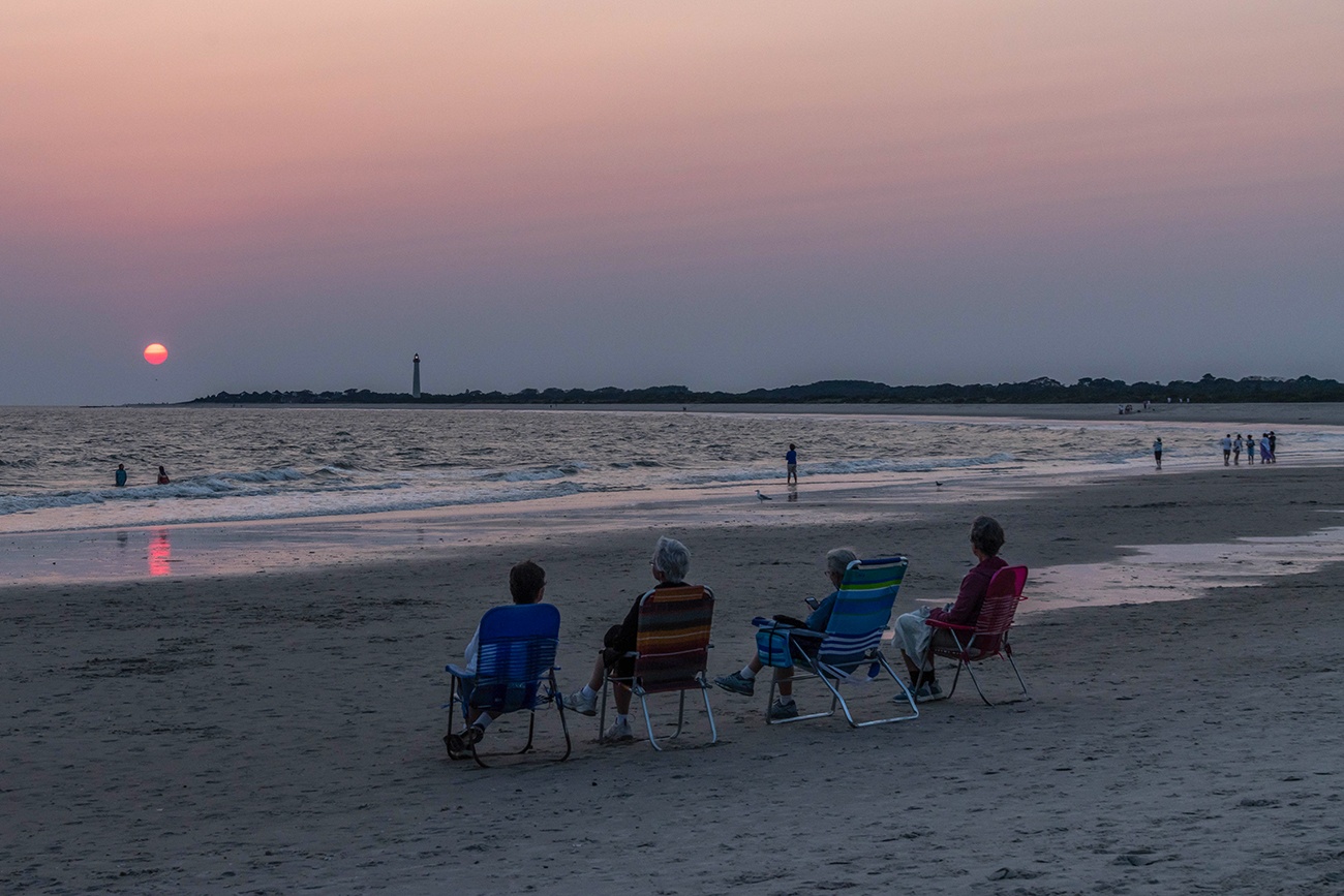 Four people sitting on the beach watching the sun set with the Cape May Lighthouse in the distance