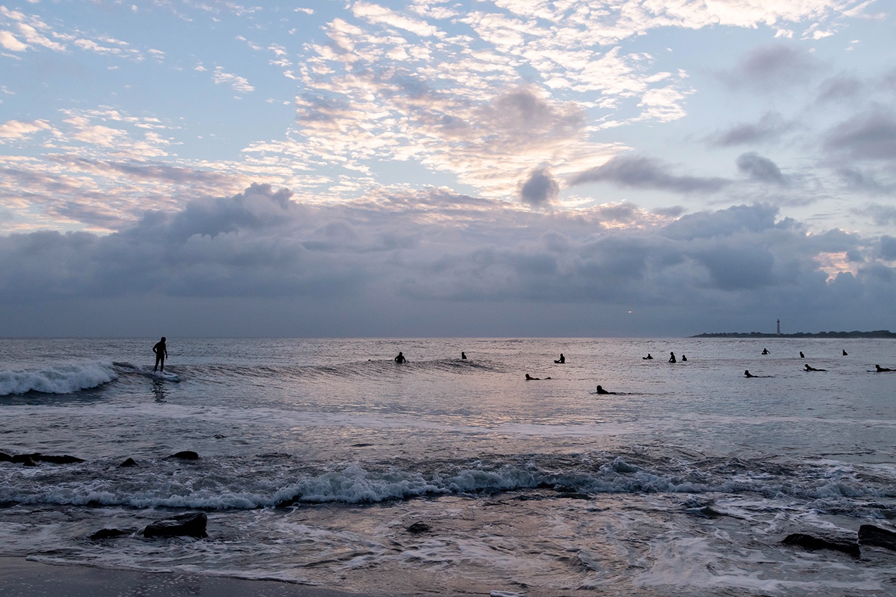 Surfers out in the ocean with clouds in the sky at sunset