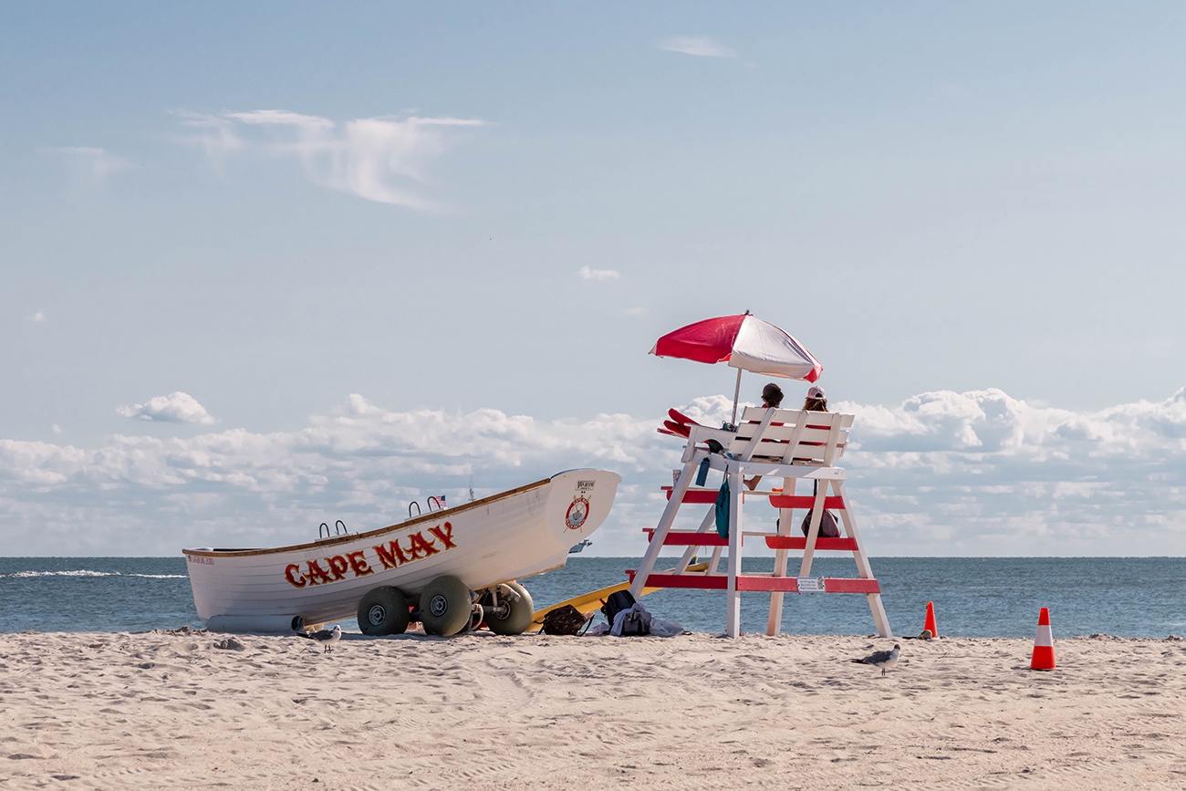 Two lifeguards sitting on a lifeguard stand with an umbrella and a Cape May lifeguard boat on the beach on a clear blue sunny day