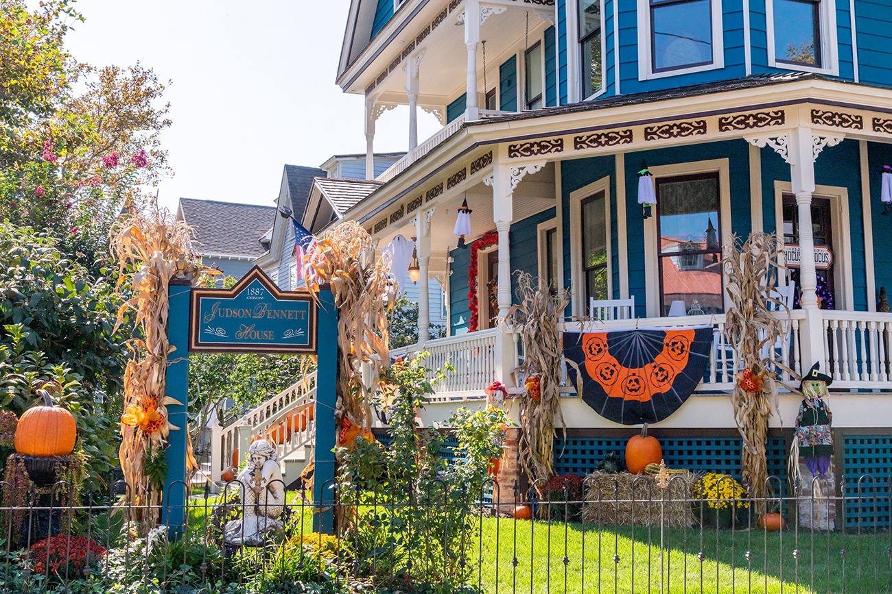 A teal Victorian house with Halloween decorations and pumpkins on a sunny day