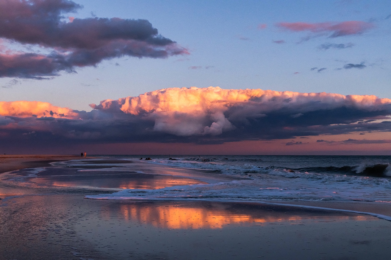 Pink and purple clouds at sunset reflected in the ocean and shoreline