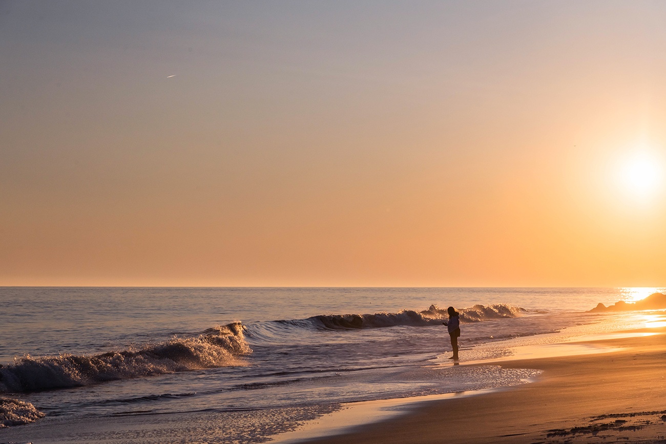 A person looking out at the ocean at sunset with waves crashing