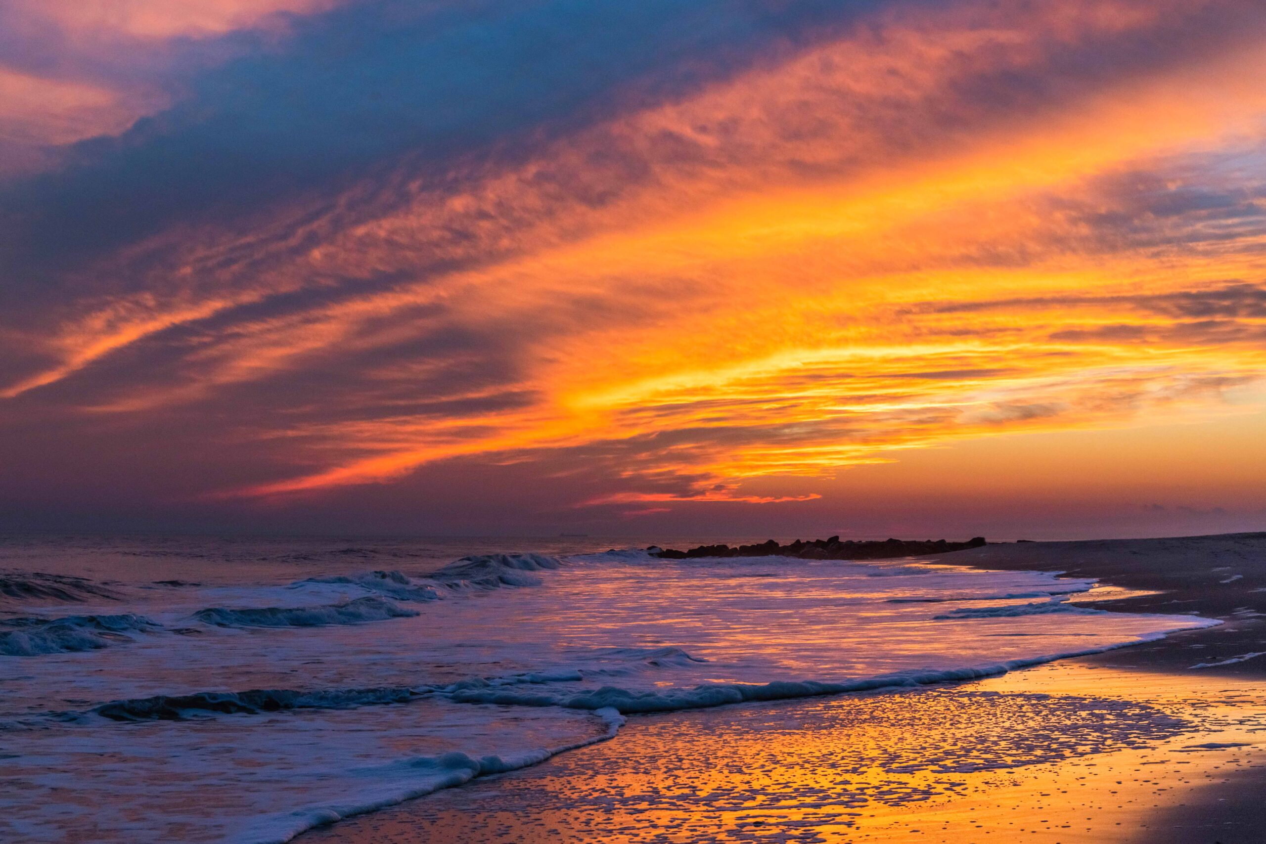 Orange, pink, and blue clouds in the sky at sunset with the colors reflected in the ocean at the beach