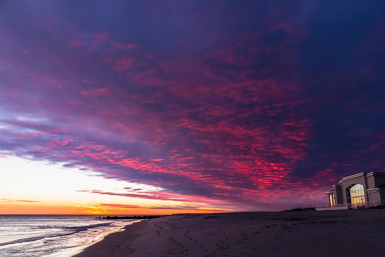 Pink and purple clouds in the sky after sunset at the beach with Convention Hall in the distance