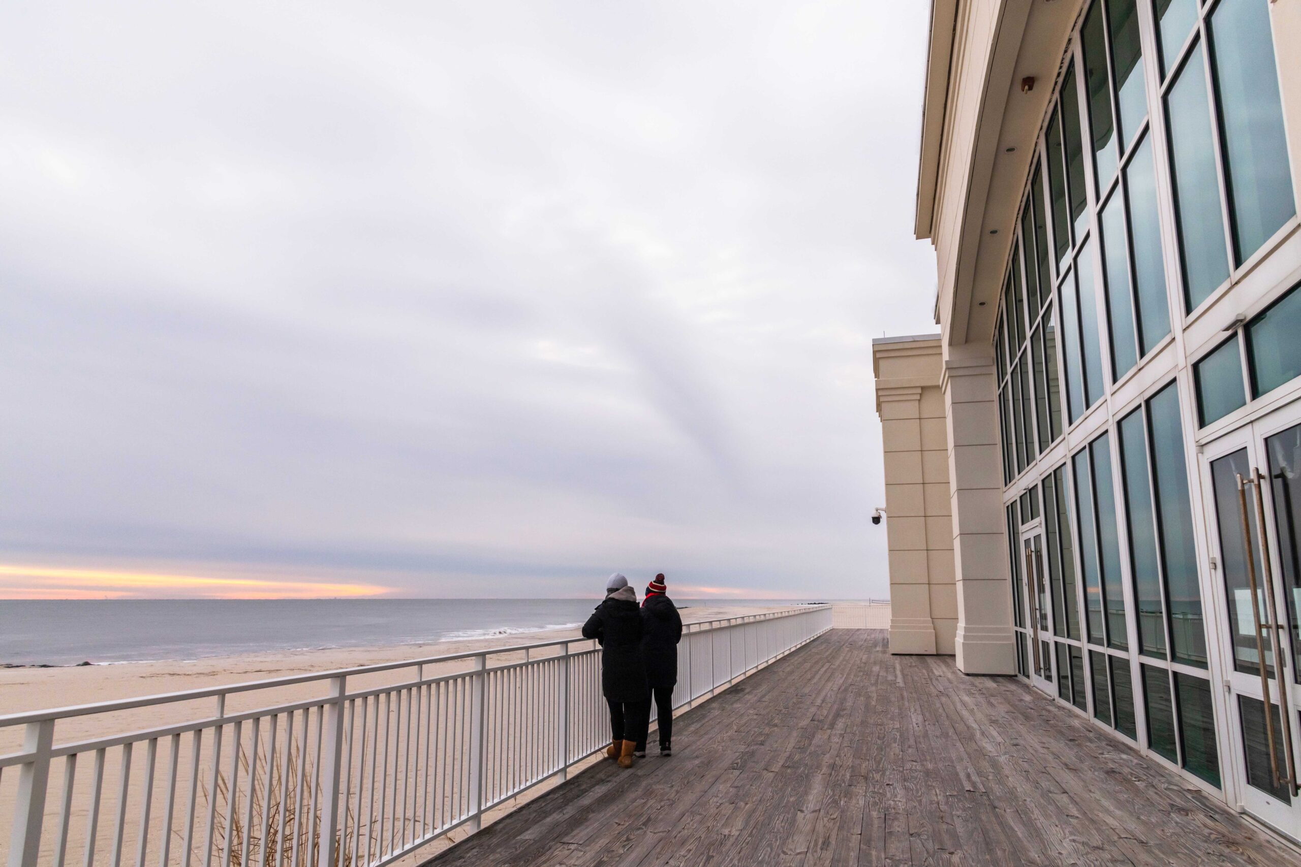 Two people standing on the deck at Convention Hall looking out to the ocean and the beach on a cloudy day
