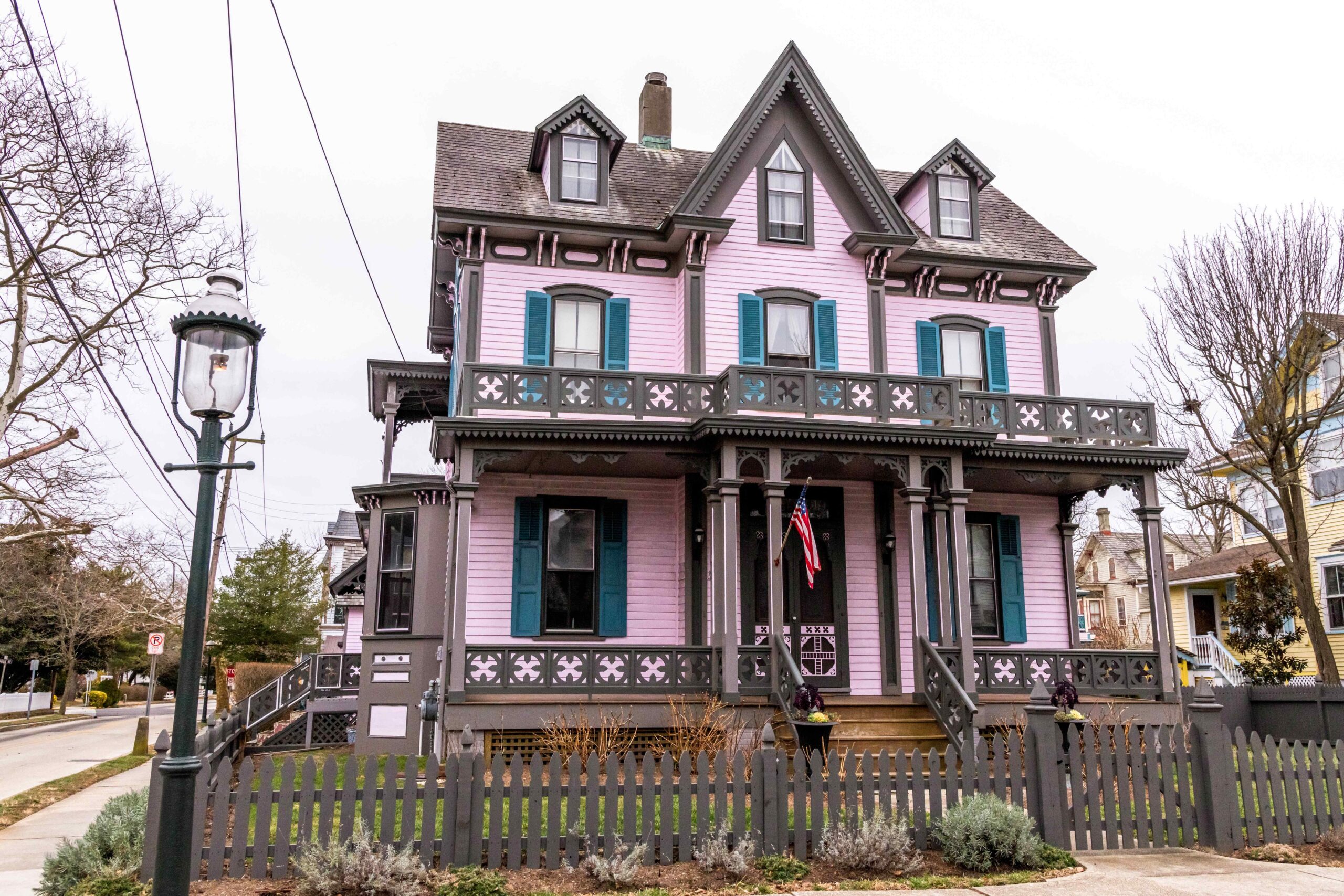 A pink, brown, and teal Victorian style house with a cloudy gray sky