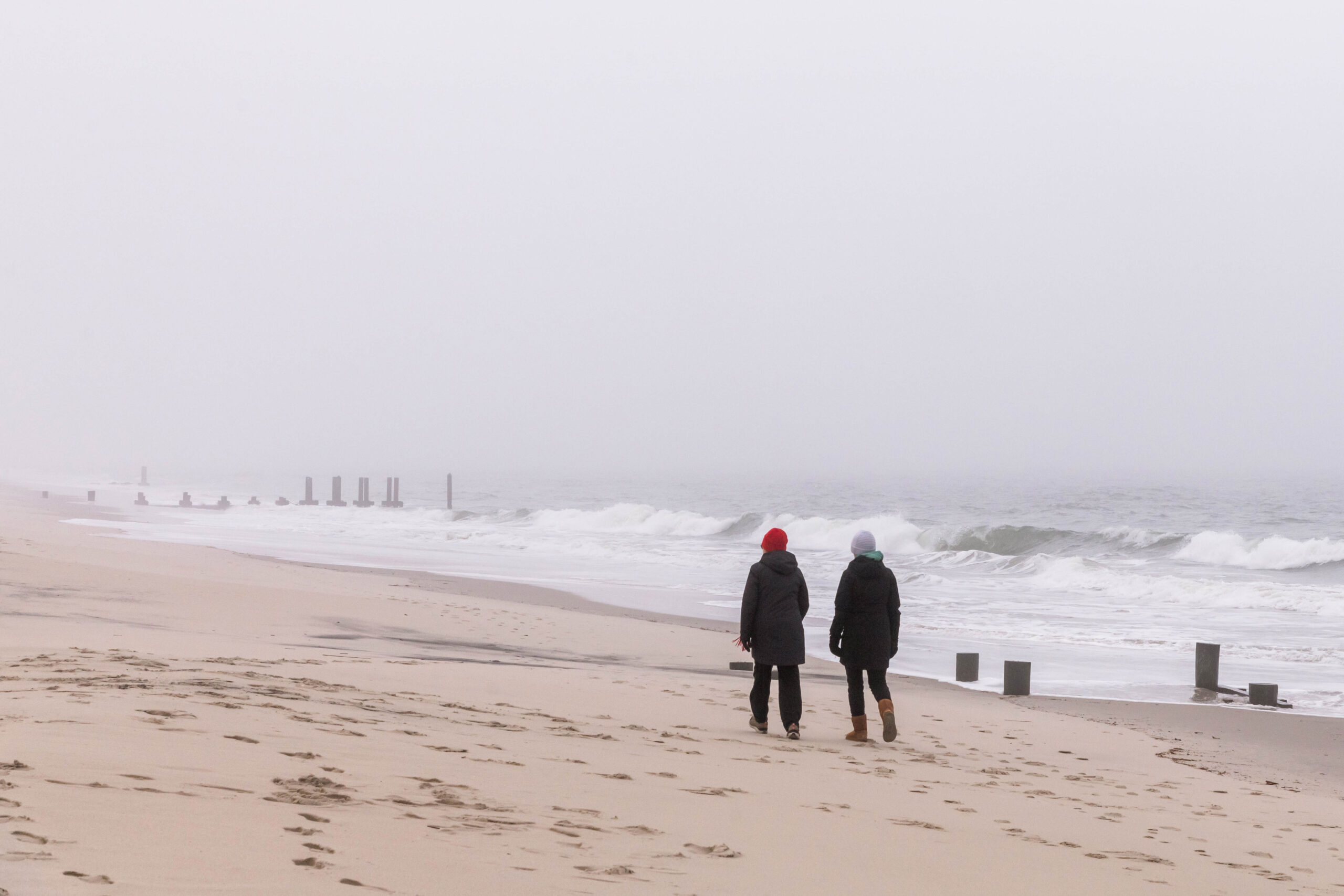 Two people walking on the beach on a foggy rainy day with waves crashing in the background