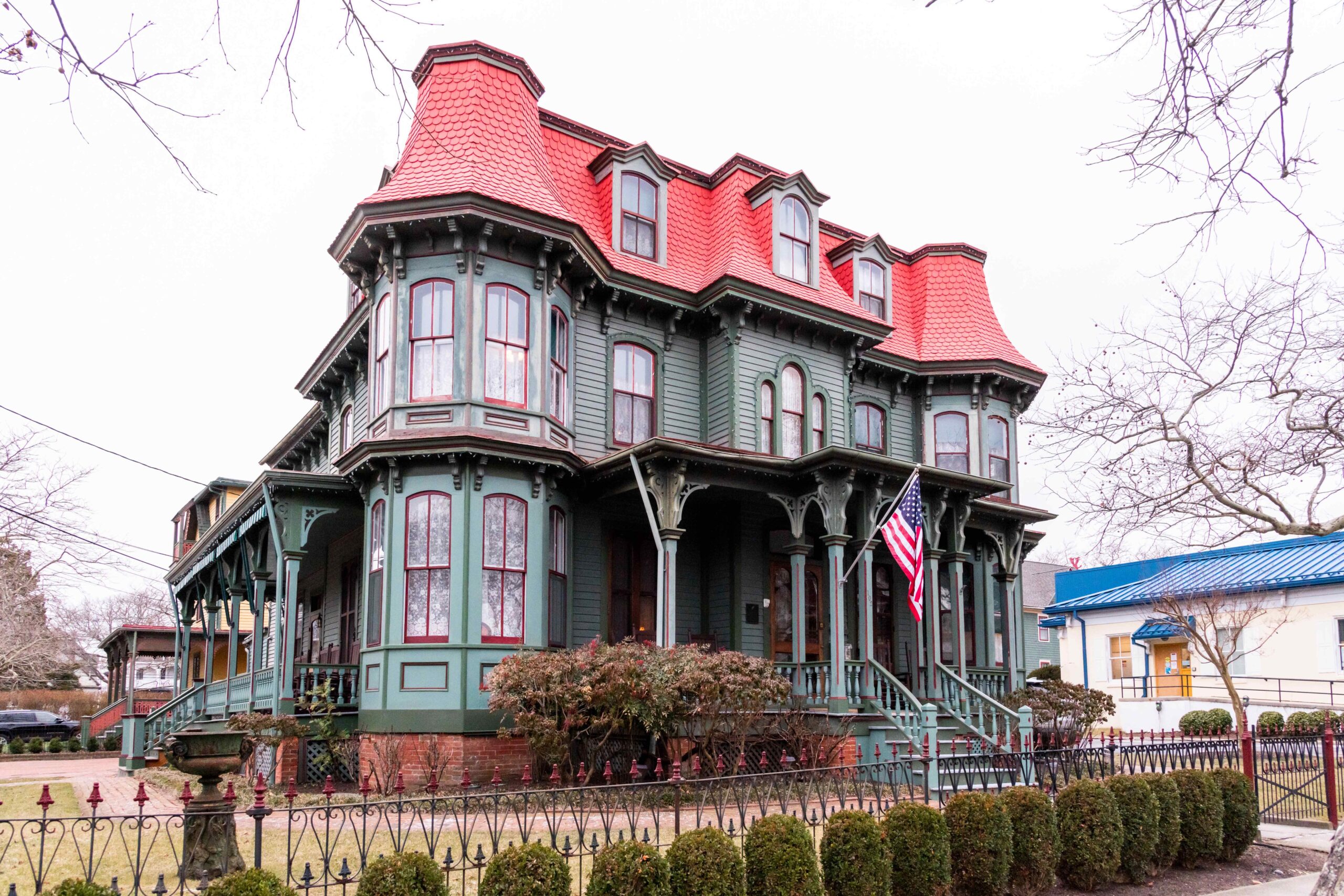 The Queen Victoria, a Victorian style bed and breakfast with green siding and a red roof, with a cloudy gray sky and bare branch trees around