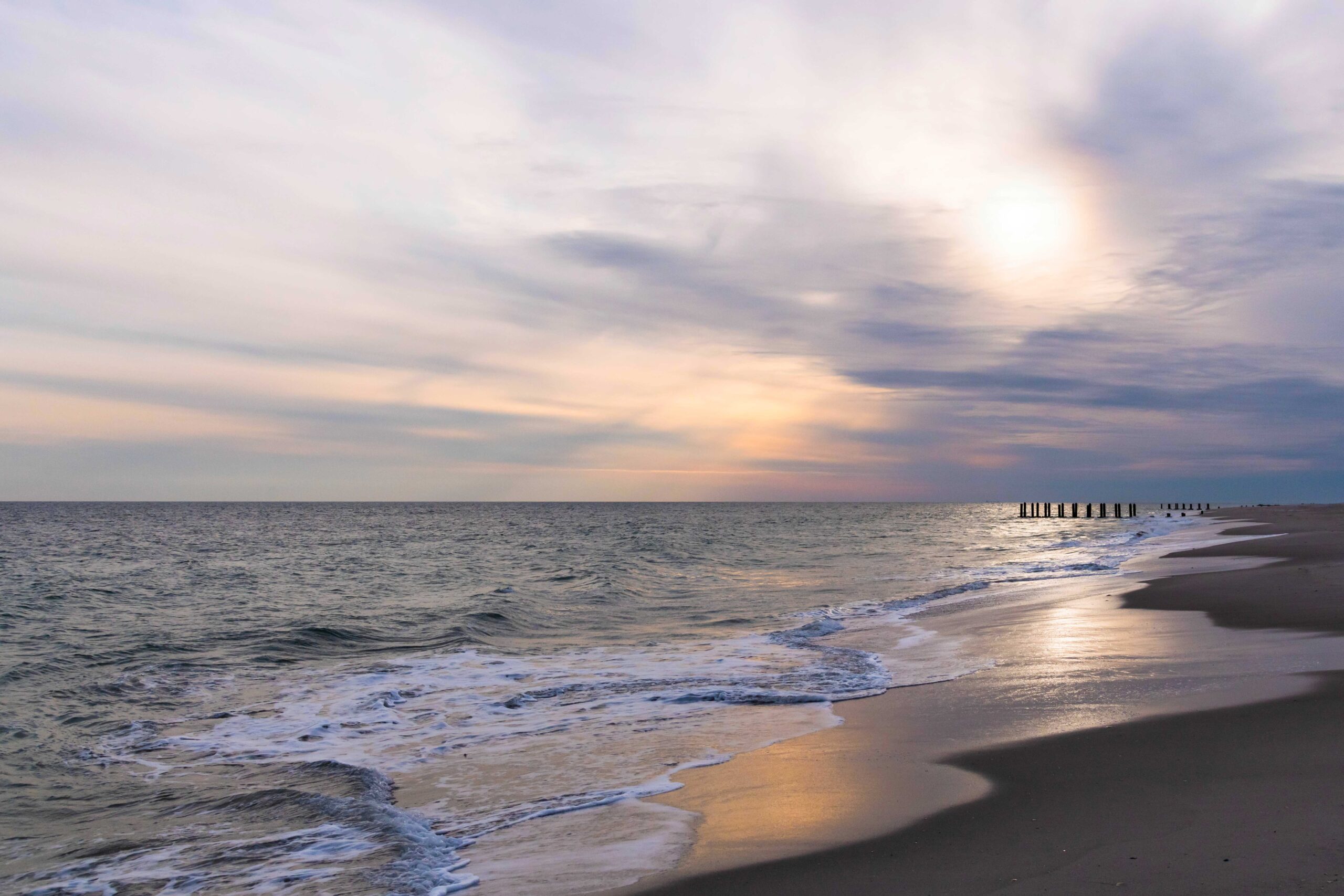 Sun filtering through a cloudy sky with small waves rolling in at the beach