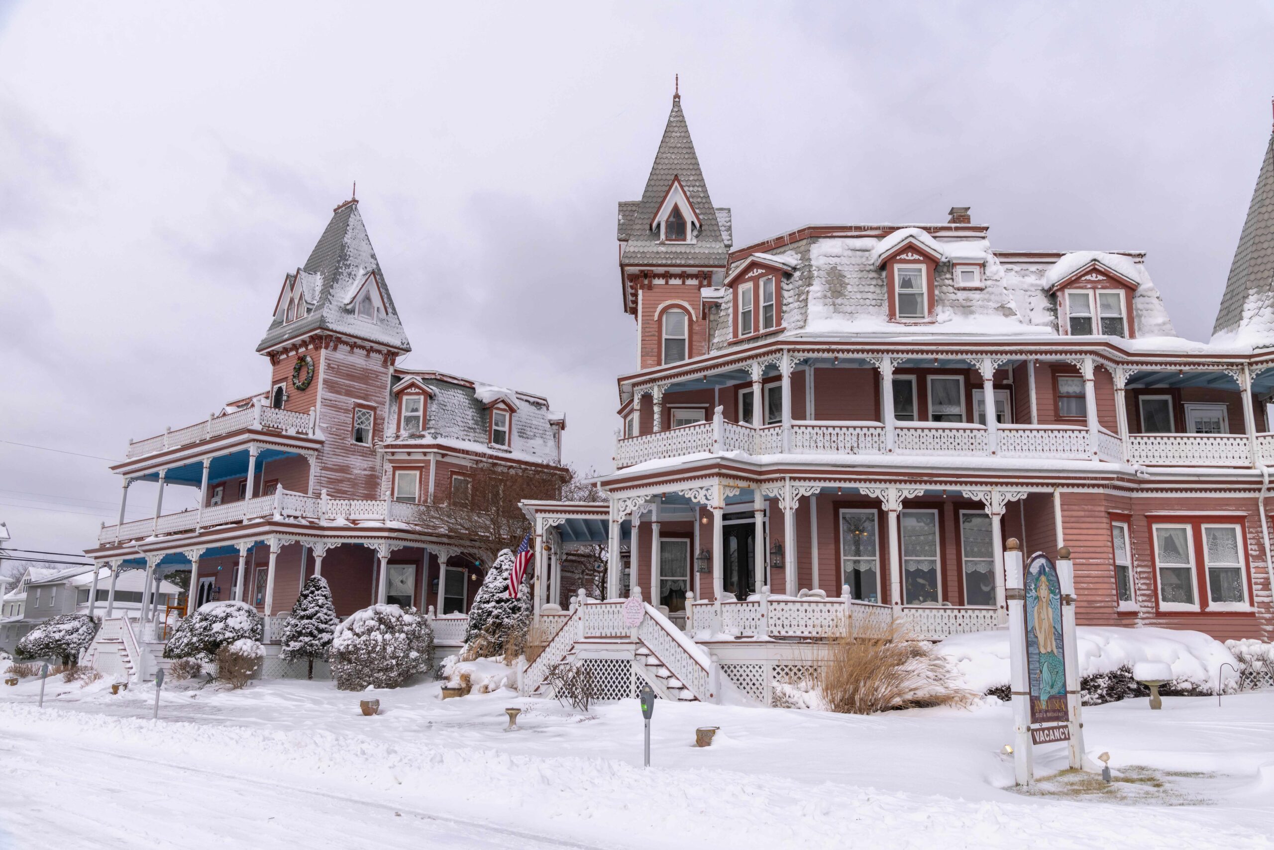 Angel of the Sea (two Victorian styled bed and breakfasts with pink and red siding) covered in snow with a cloudy sky