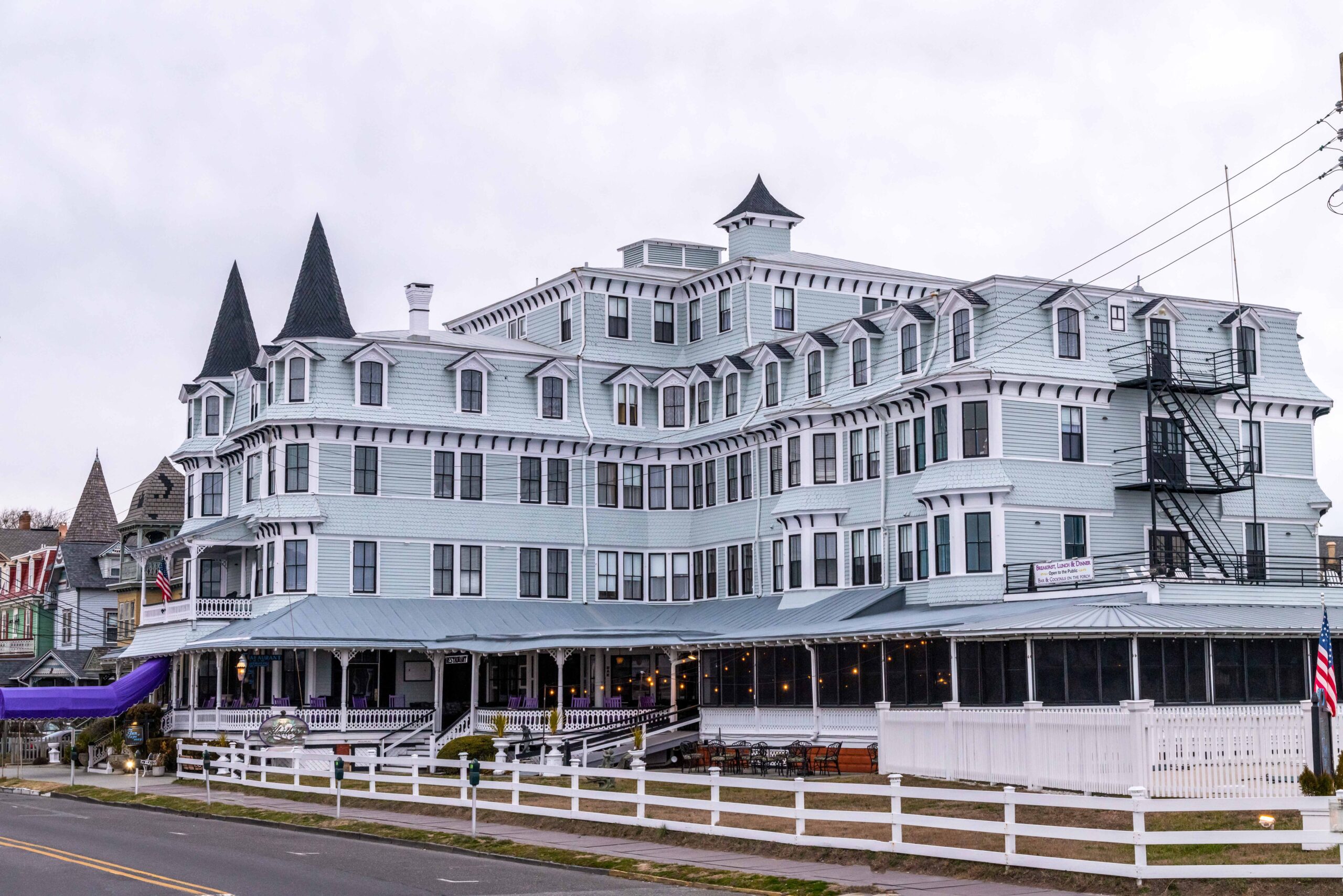 The Inn of Cape May (a Victorian style gray building with a purple awning) with a cloudy gray sky