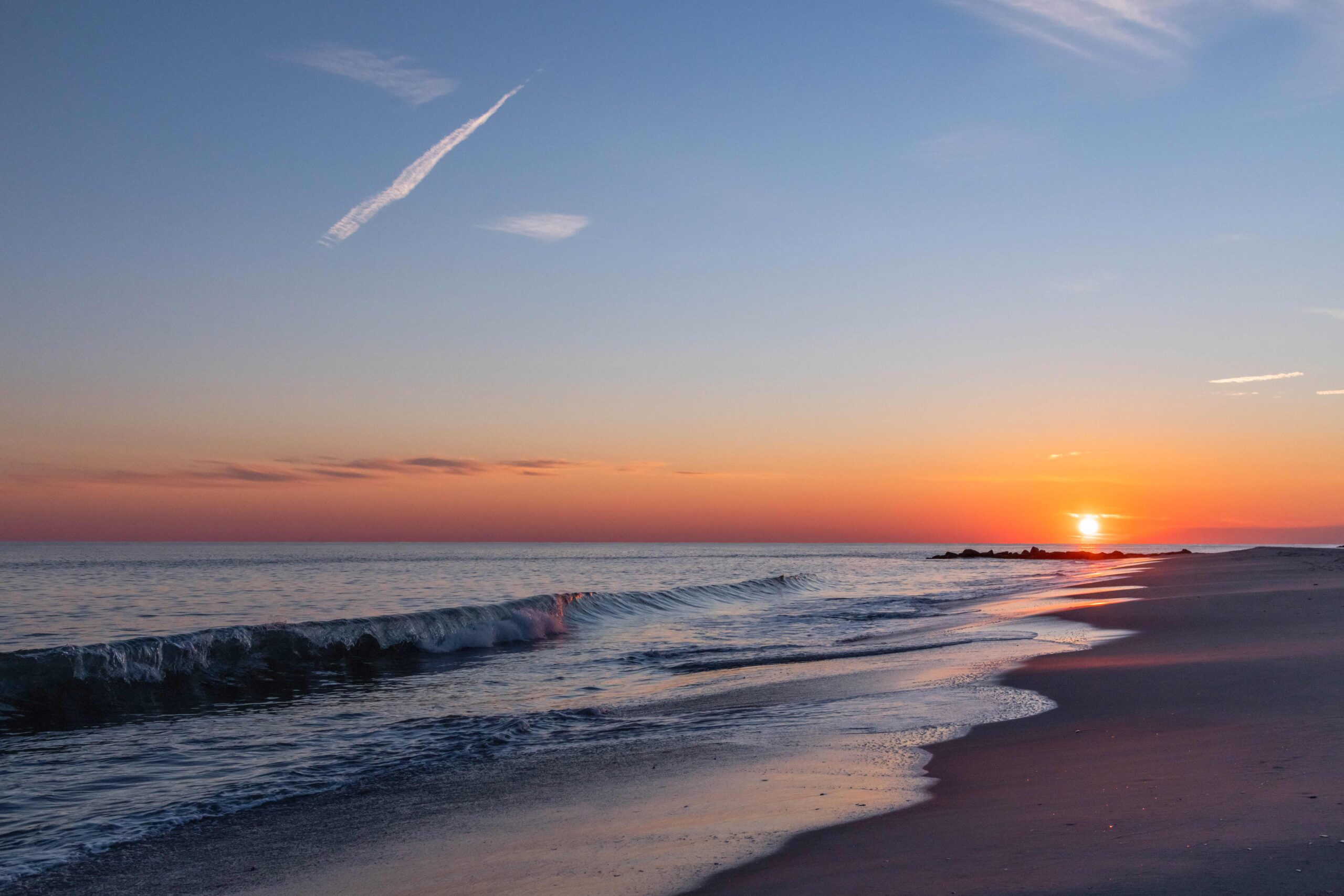 The sun setting as a single wave crashes at the beach with a clear sky