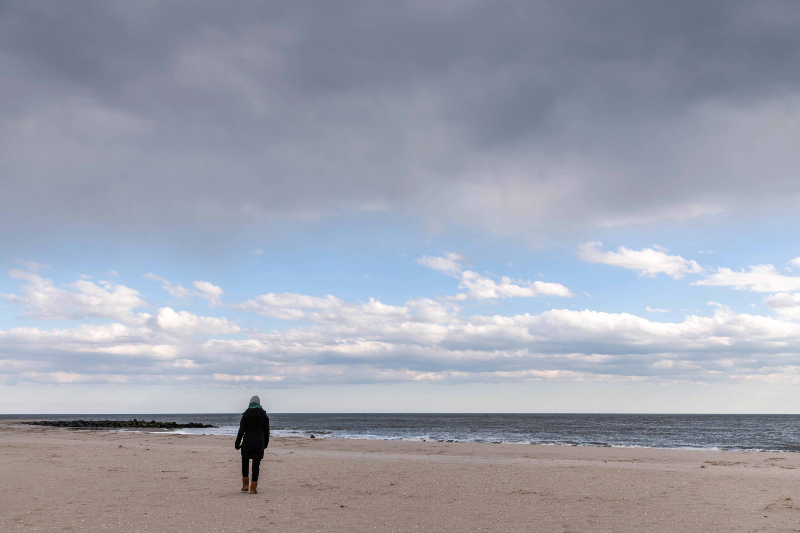 A person walking on the beach with dark puffy clouds and blue sky
