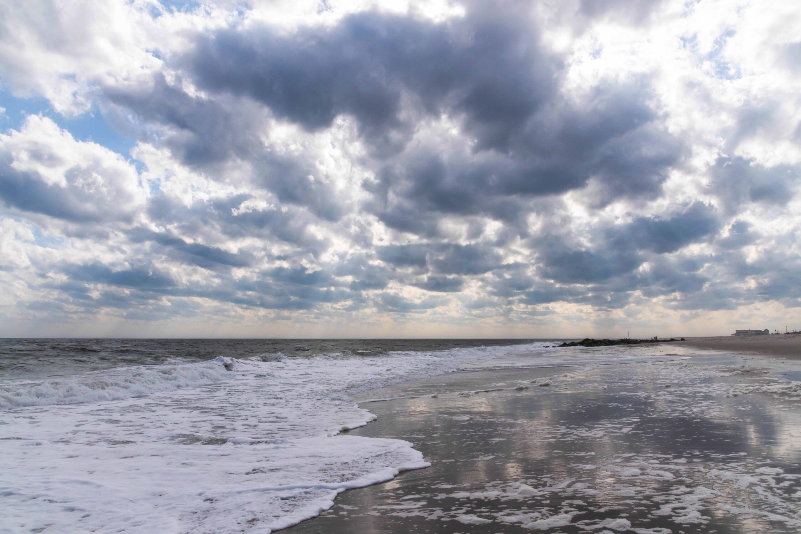 Puffy dark blue and white clouds in the sky with the ocean rushing into the shore at the beach