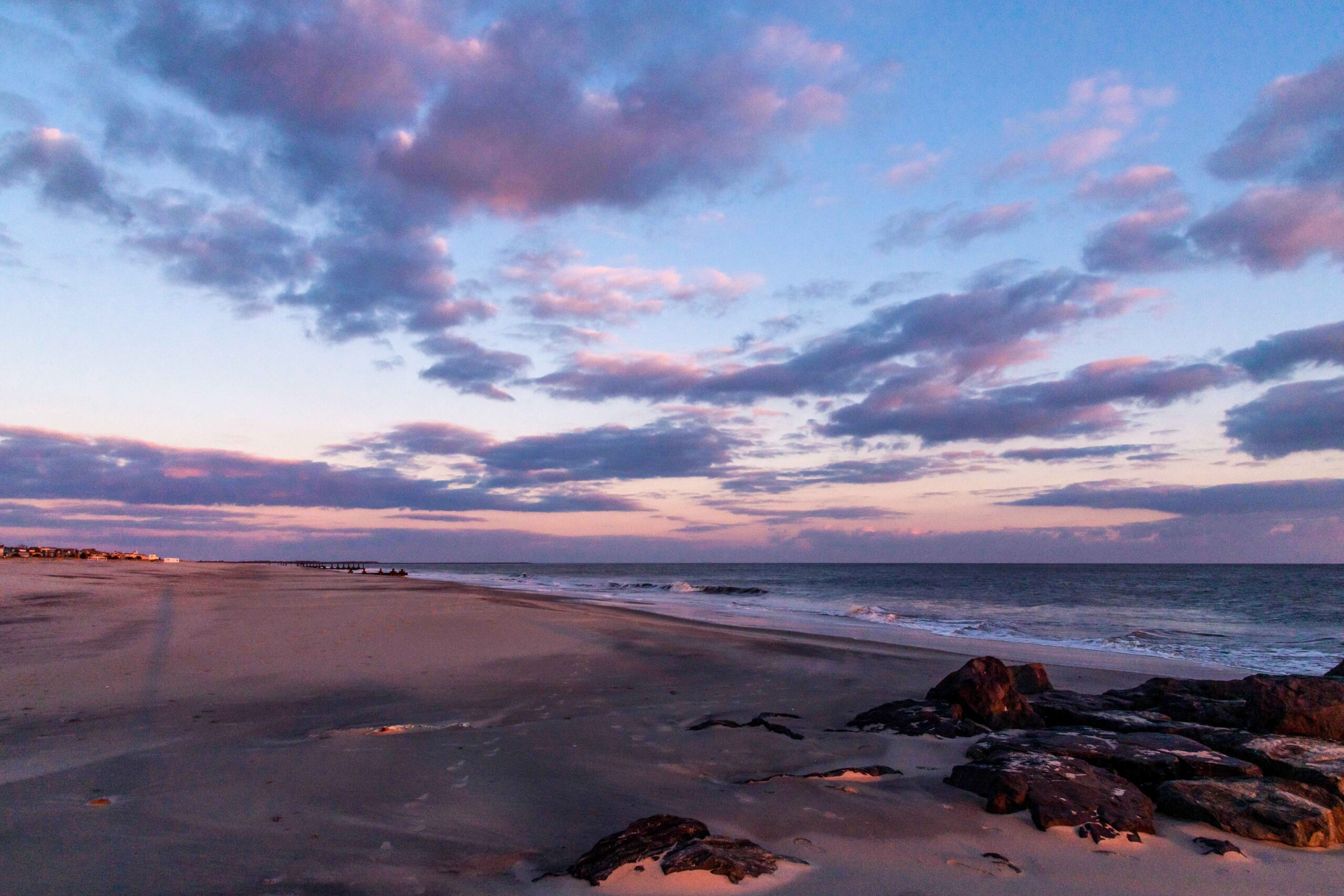 Pink and purple clouds in a blue sky at sunset with golden light reflected on the sand and in the rocks at the beach