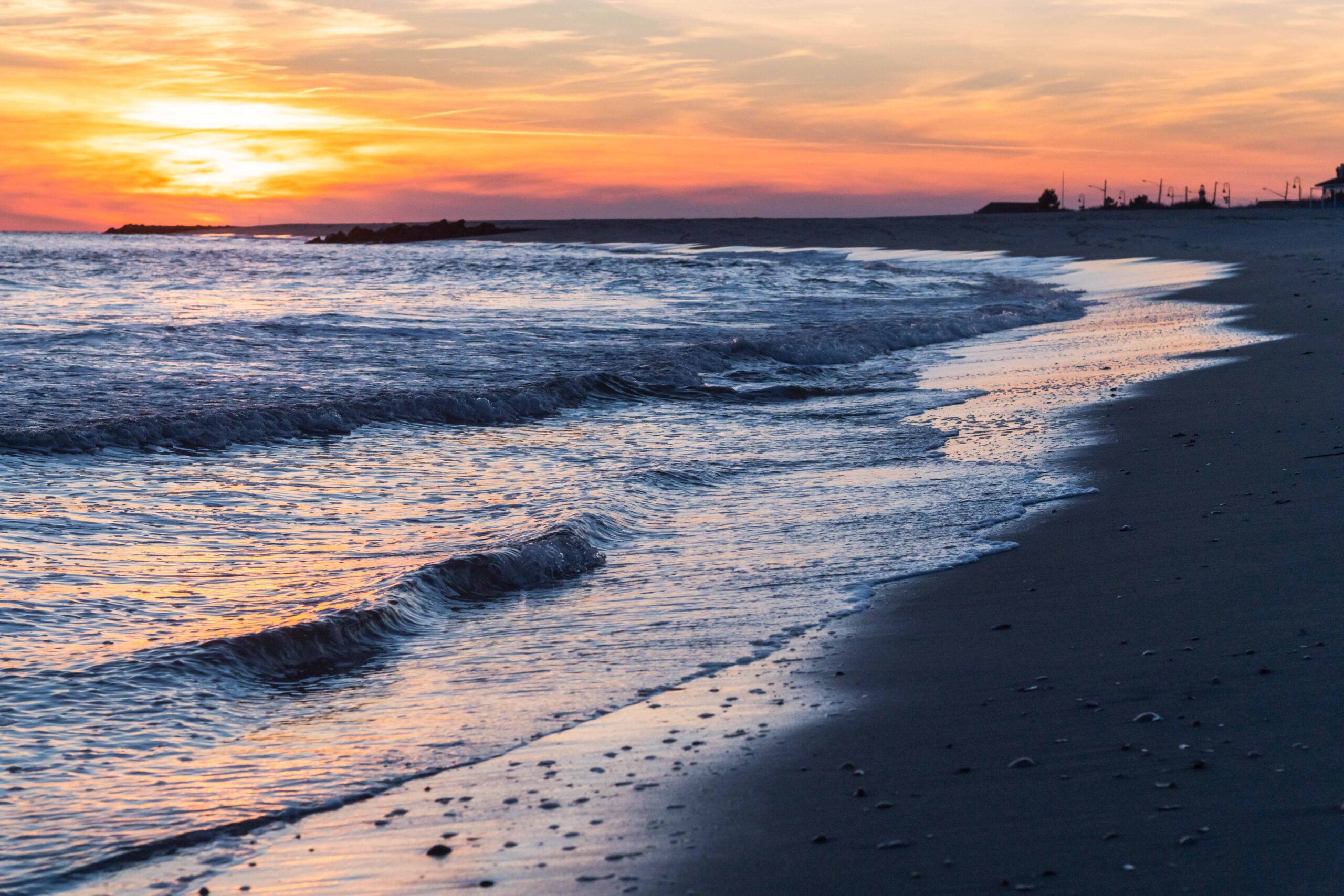 Orange and pink clouds in the sky at sunset with small waves in the foreground at the shoreline