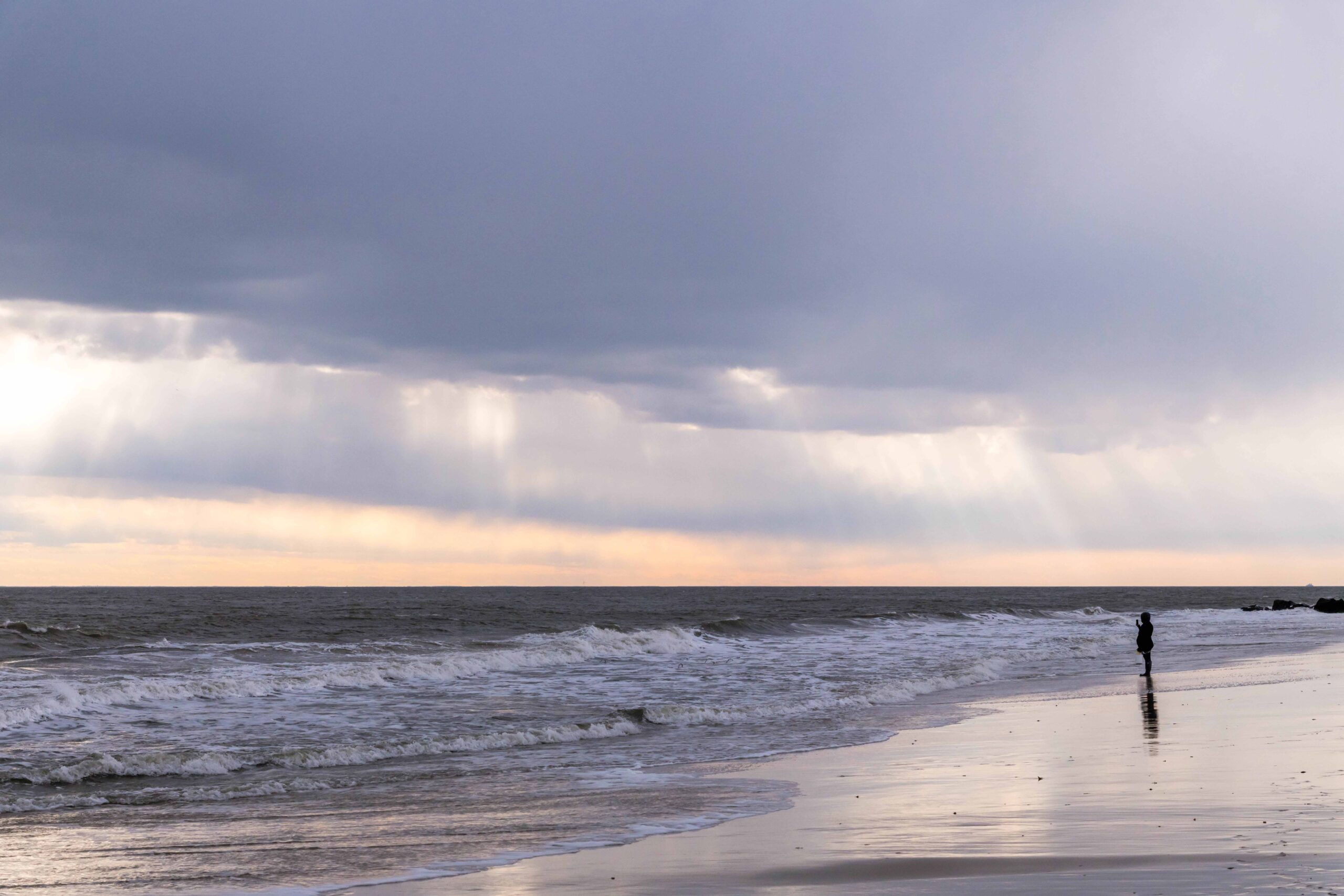 Sunlight filtering through dark clouds in the sky with a person standing at the ocean