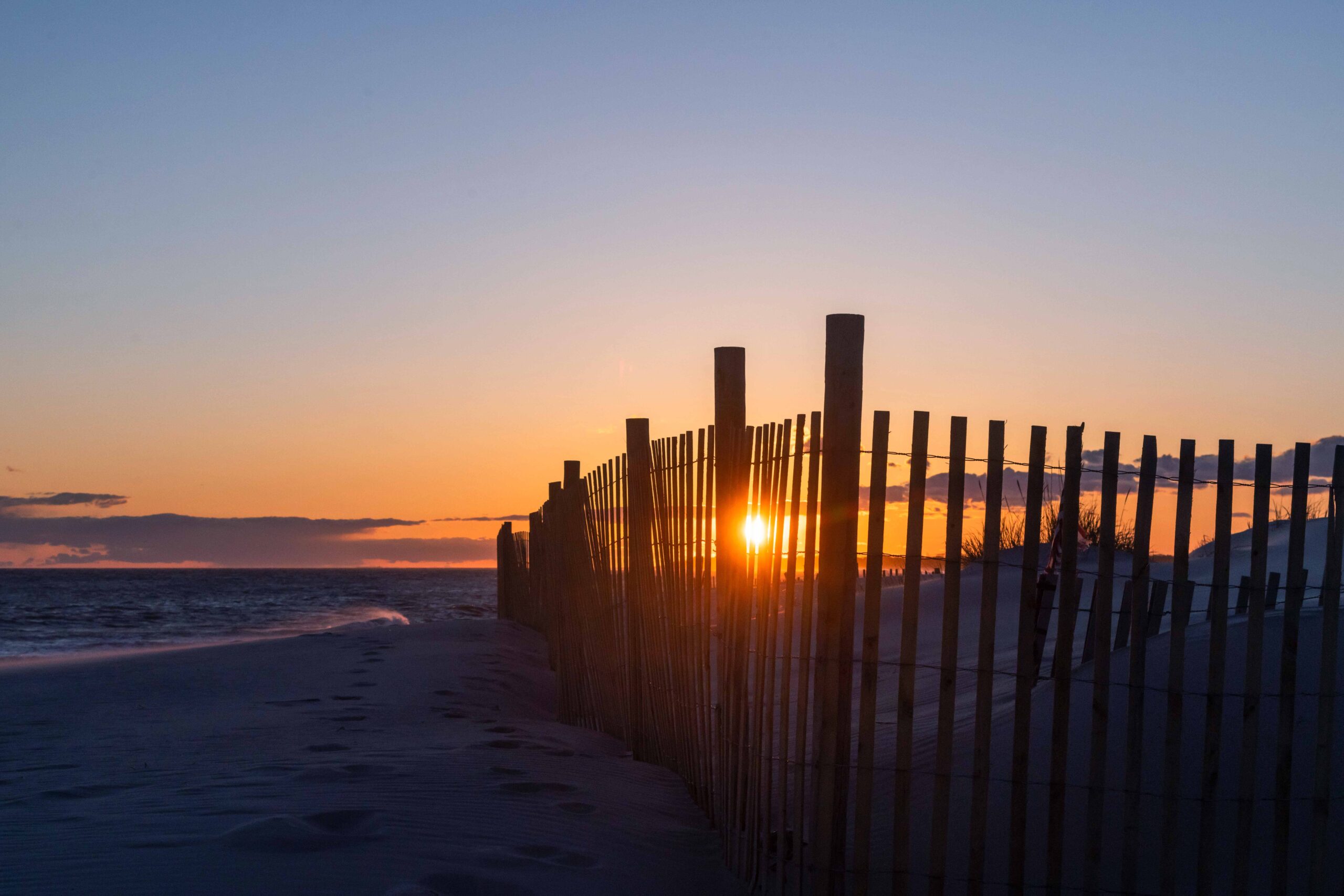 Sunset through a beach fence with a clear sky and the ocean in the background