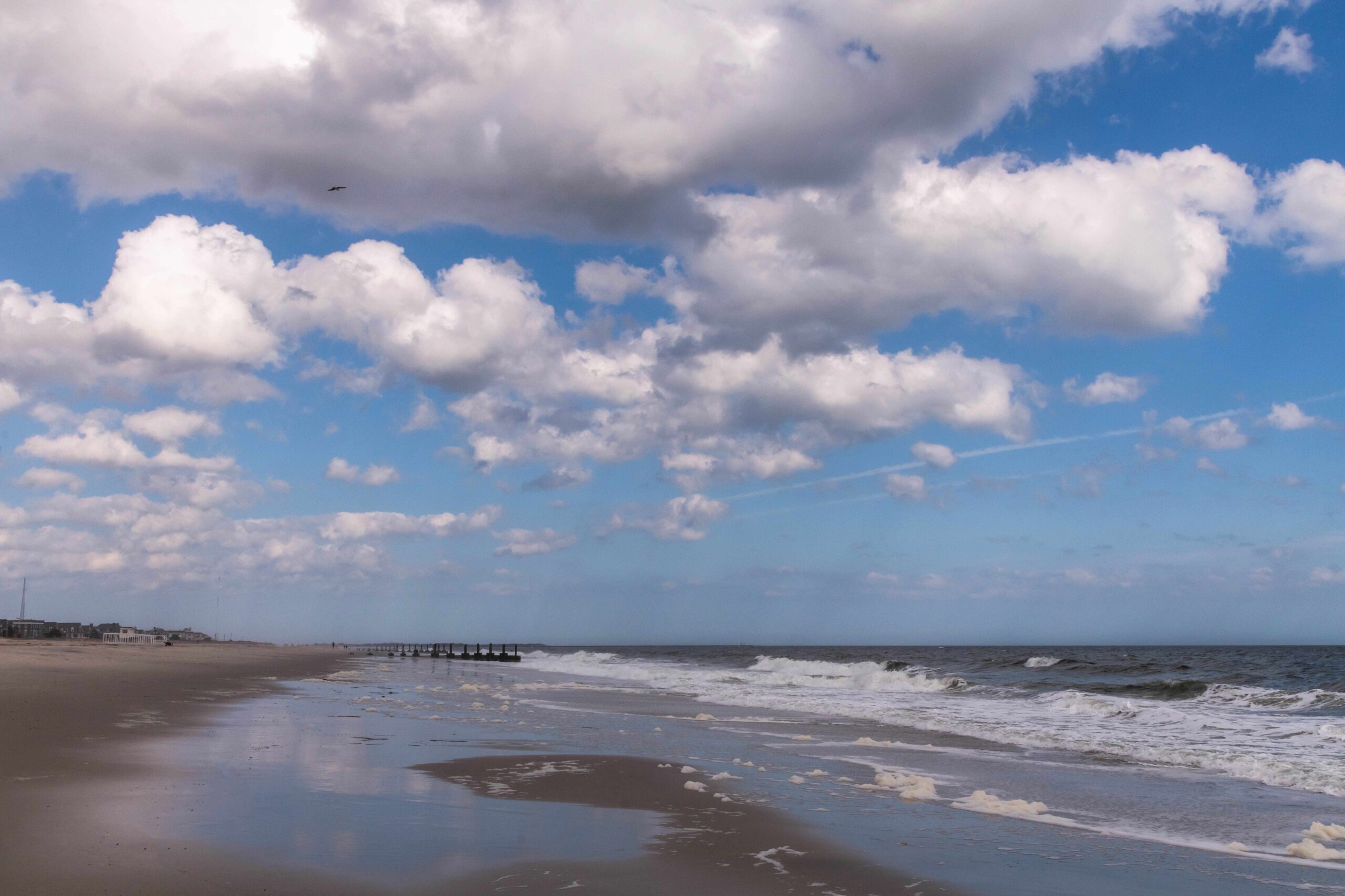 Puffy white clouds in a blue sky reflected in the sand and ocean, with waves rolling into the shoreline