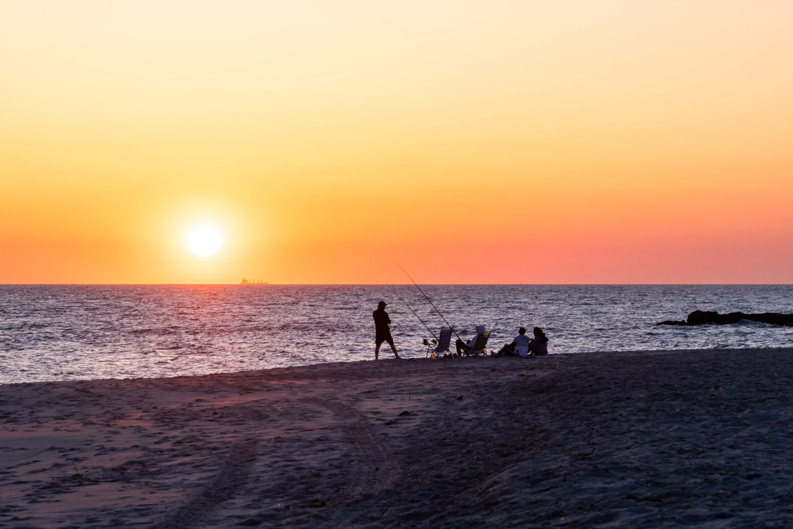 People sitting in beach chairs and fishing at the beach at sunset with a clear sky