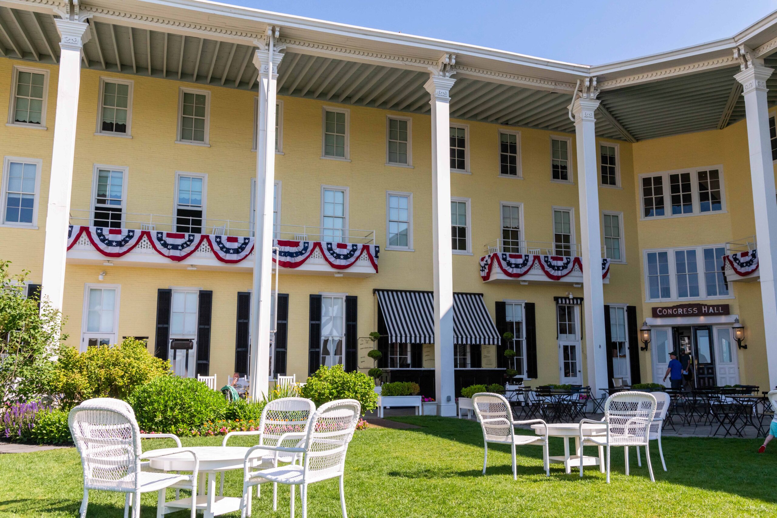 Tables and chairs on the front lawn of Congress Hall with American Flag bunting hung up on the decks of second floor rooms