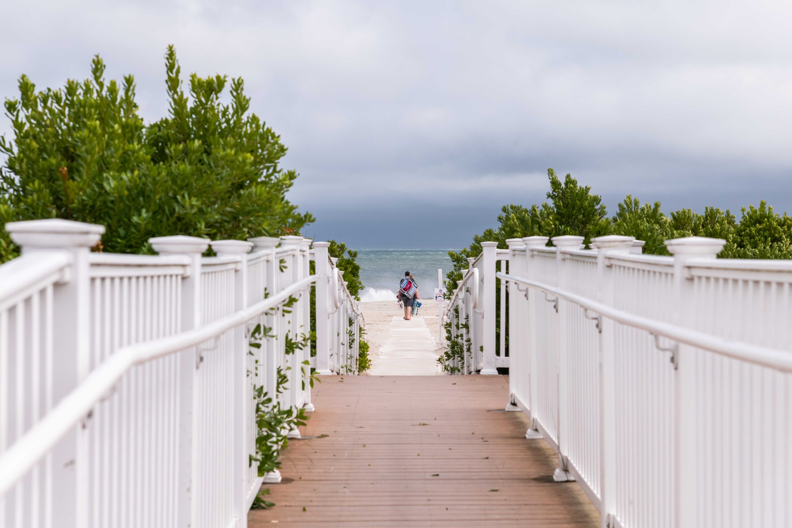 A close up view of a beach path with a person in the distance walking on the beach with a cloudy sky