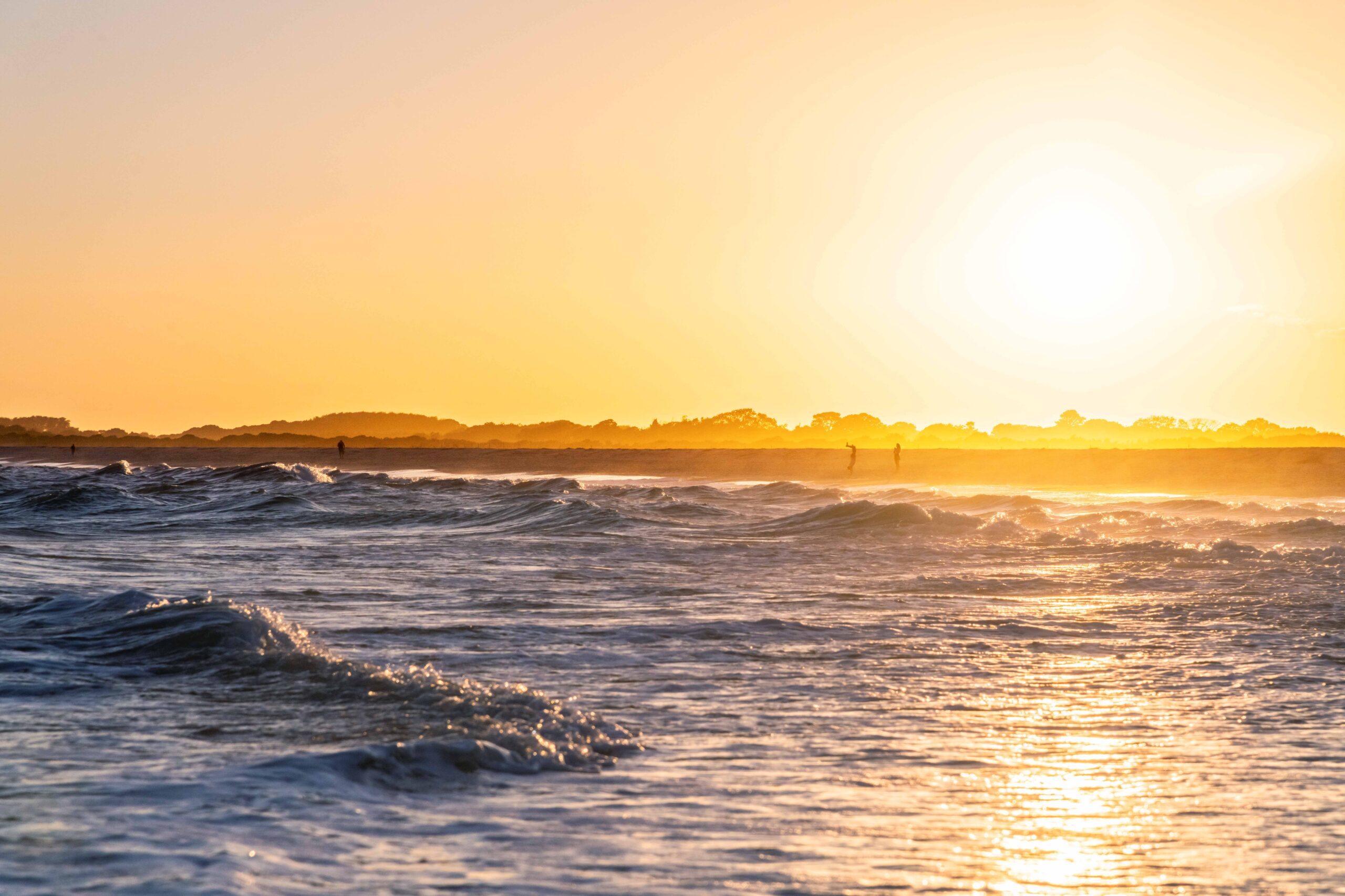 Waves rolling into the shore at sunset with people walking in the distance on the beach