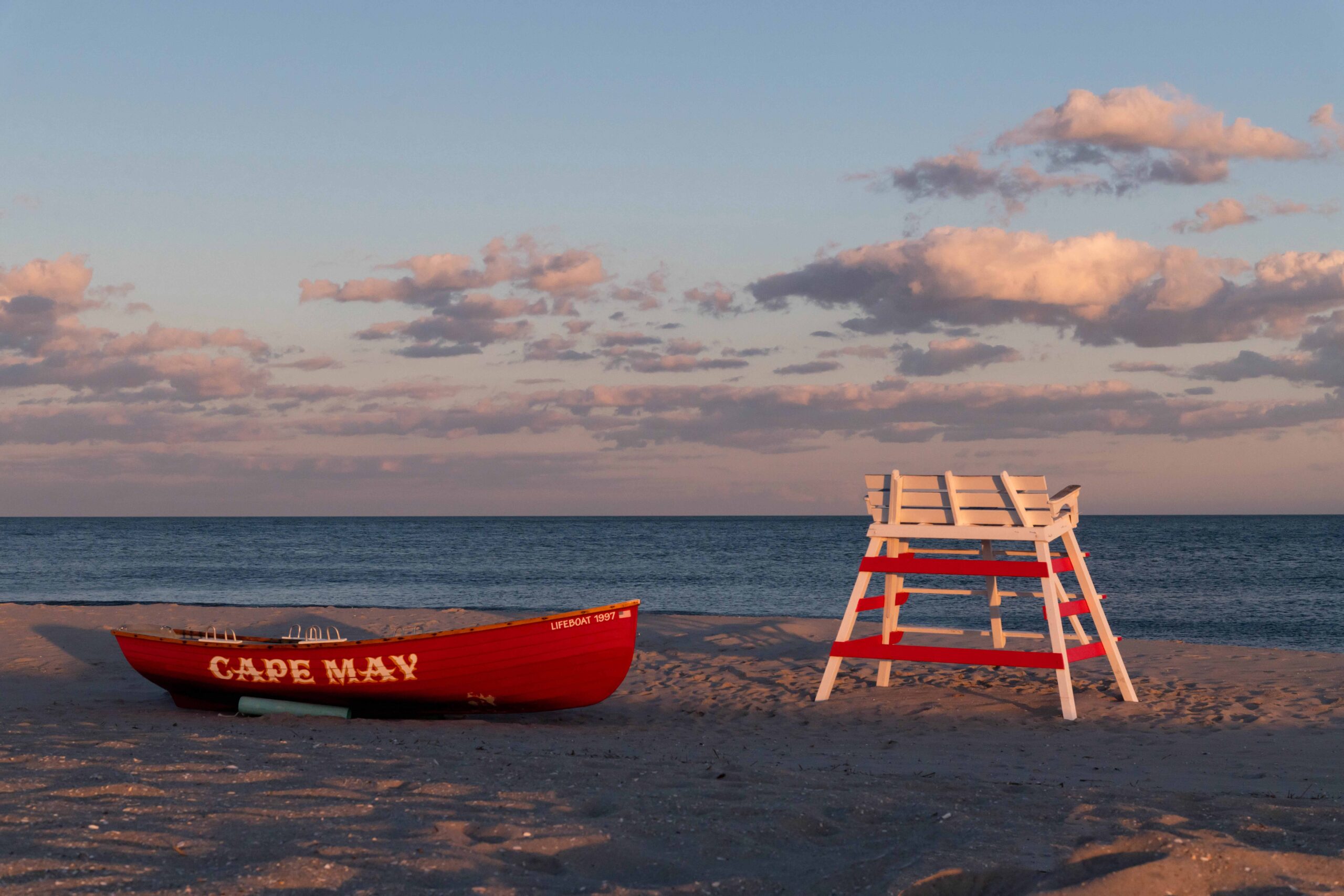 A red lifeguard Cape May boat and a lifeguard stand at sunset with the ocean and clouds in the background