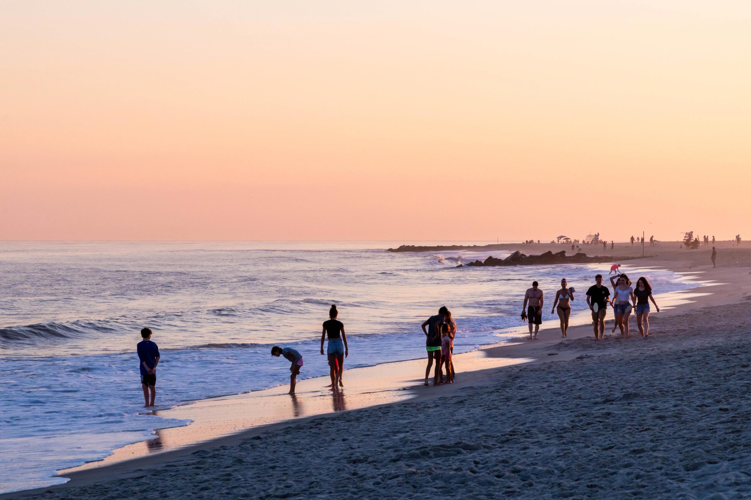 People walking along the ocean at sunset with a pink sky