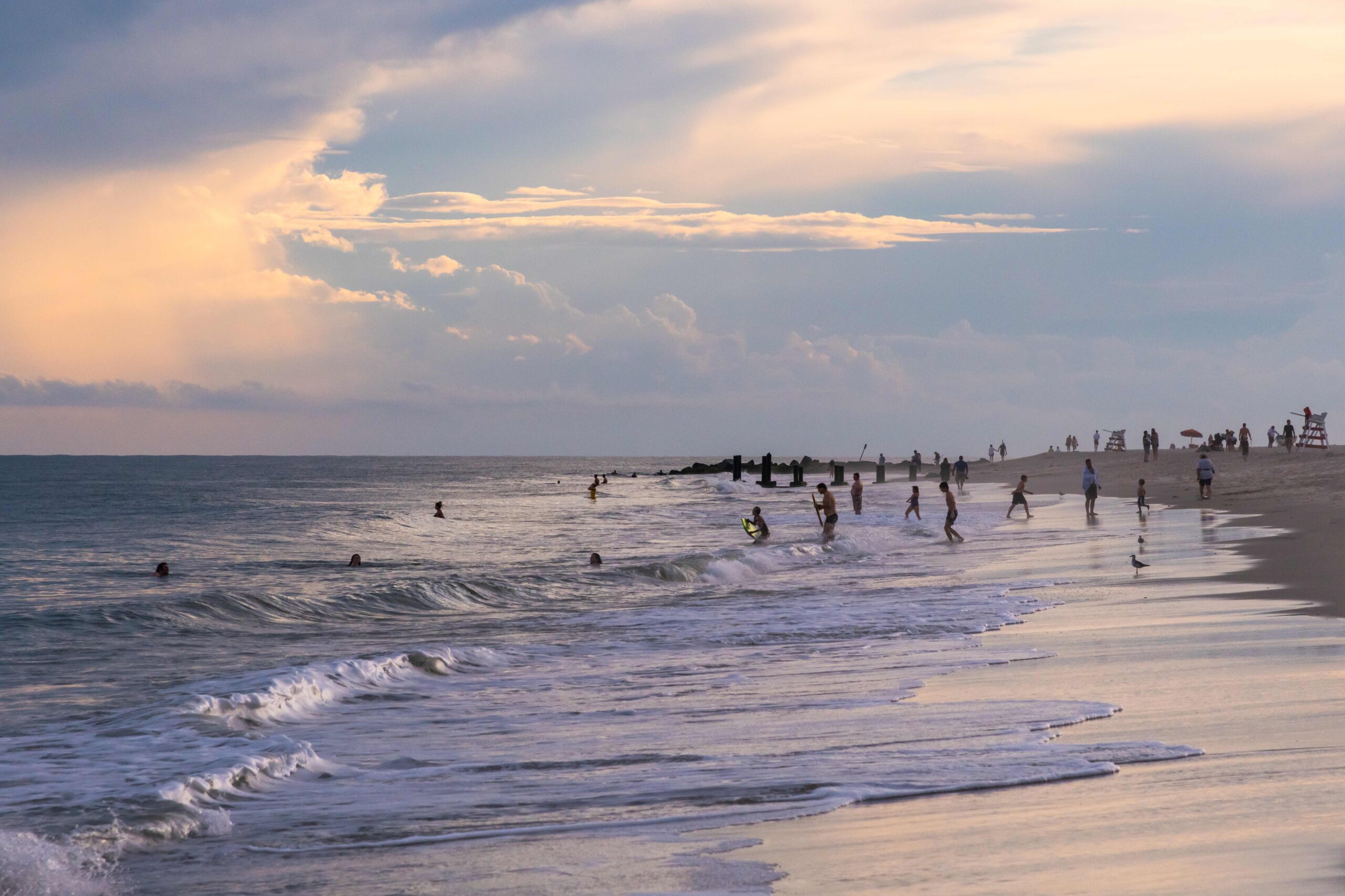 People going in the ocean at the beach at sunset with clouds in the sky