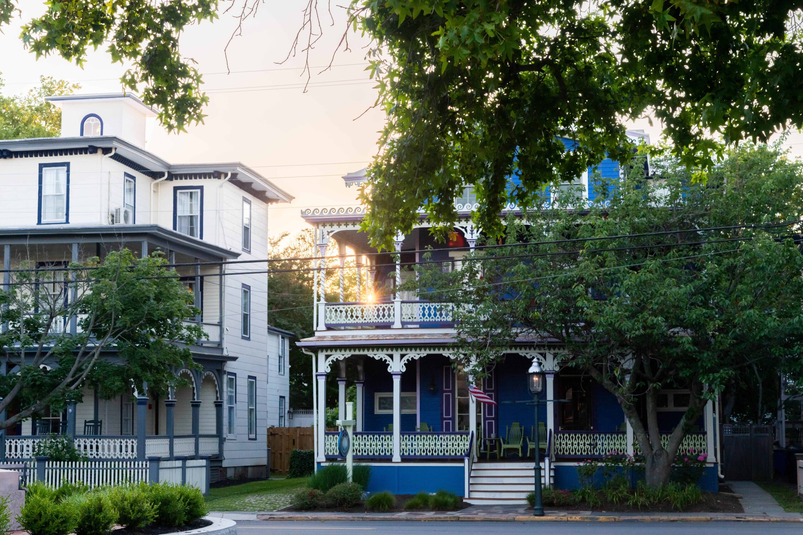 Sun setting behind a blue victorian house with green trees