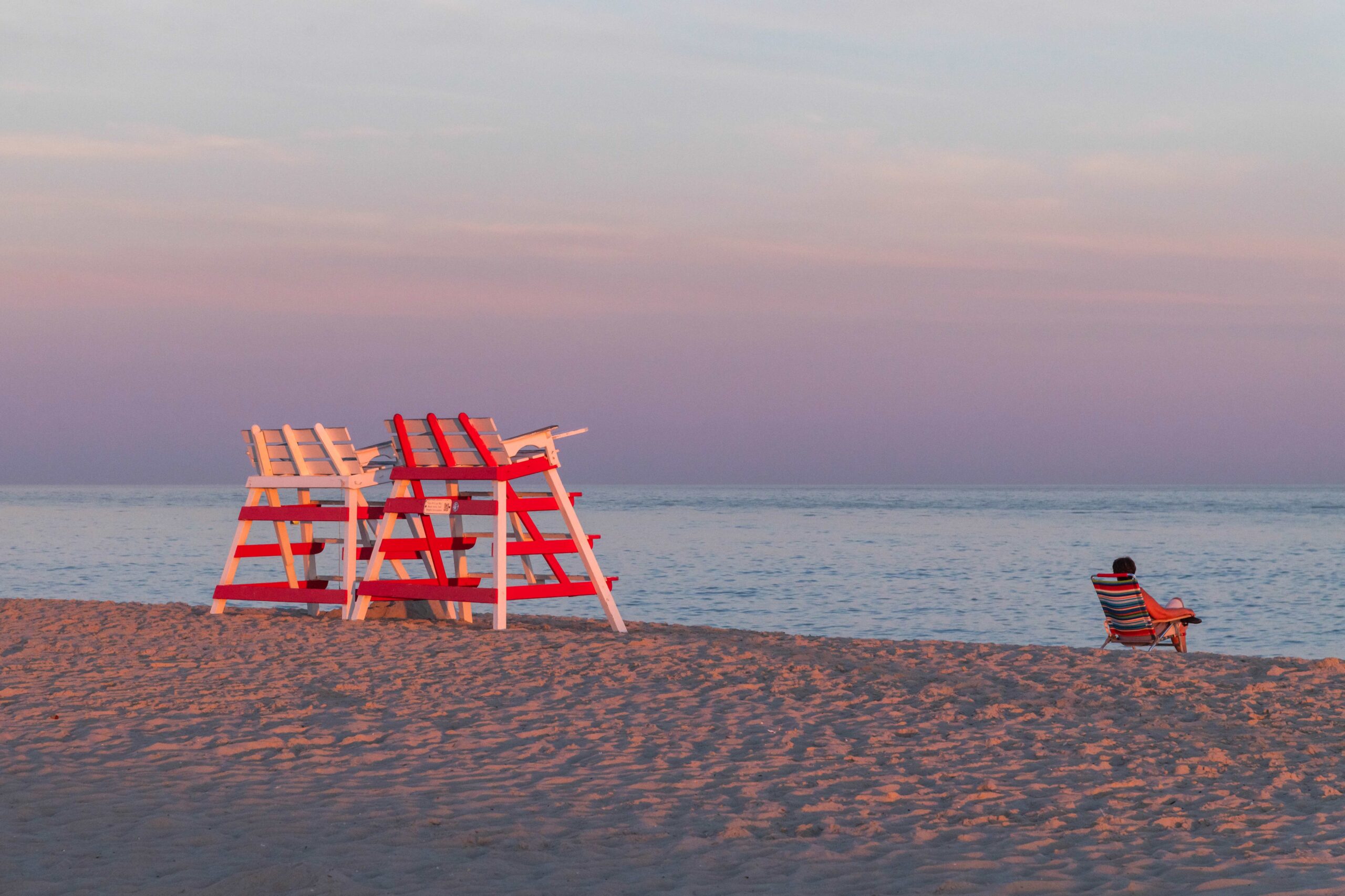 A person sitting on the beach with two lifeguard stands at sunset