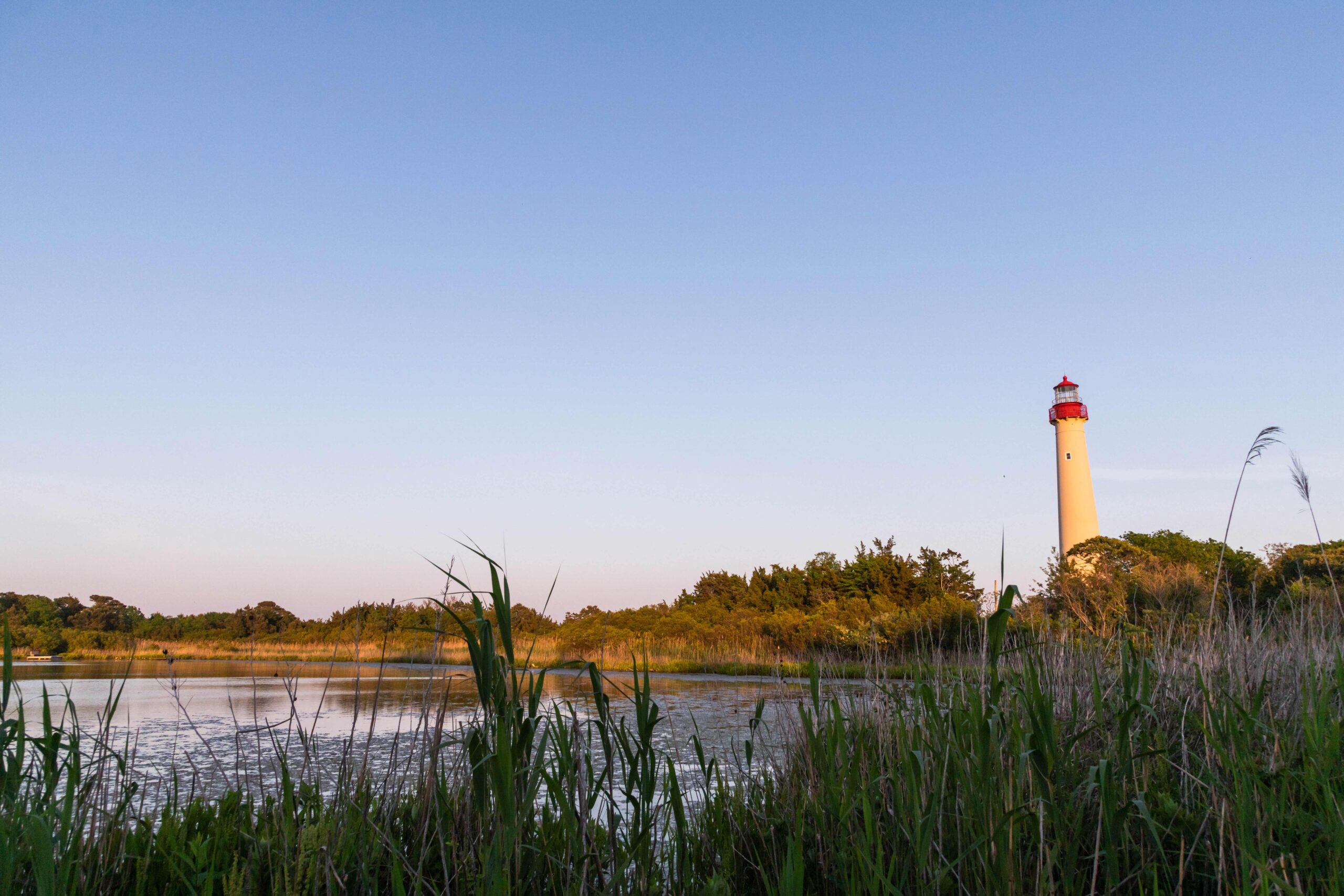 Sunset light shining on the Cape May Lighthouse and the Lighthouse Pond with a clear blue sky