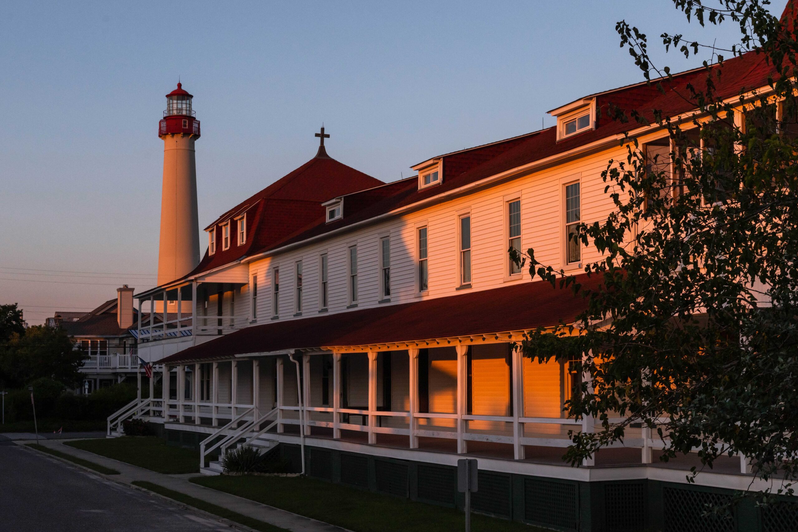 Light from sunset shining on Saint Mary By the Sea and the Cape May Lighthouse with a clear blue sky