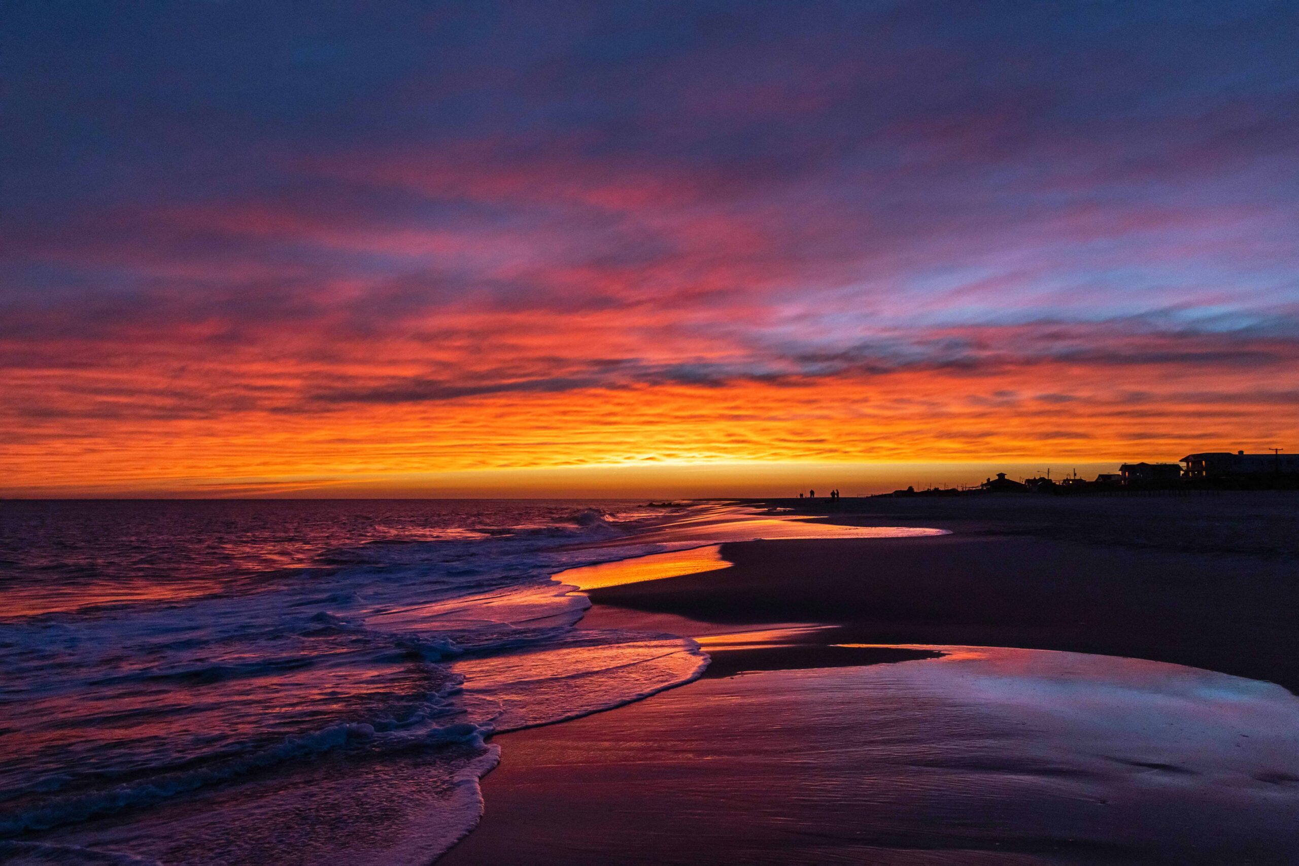 Blue, purple, red, pink, orange, and yellow colored clouds in the sky reflected in the ocean and sand at the beach at sunset