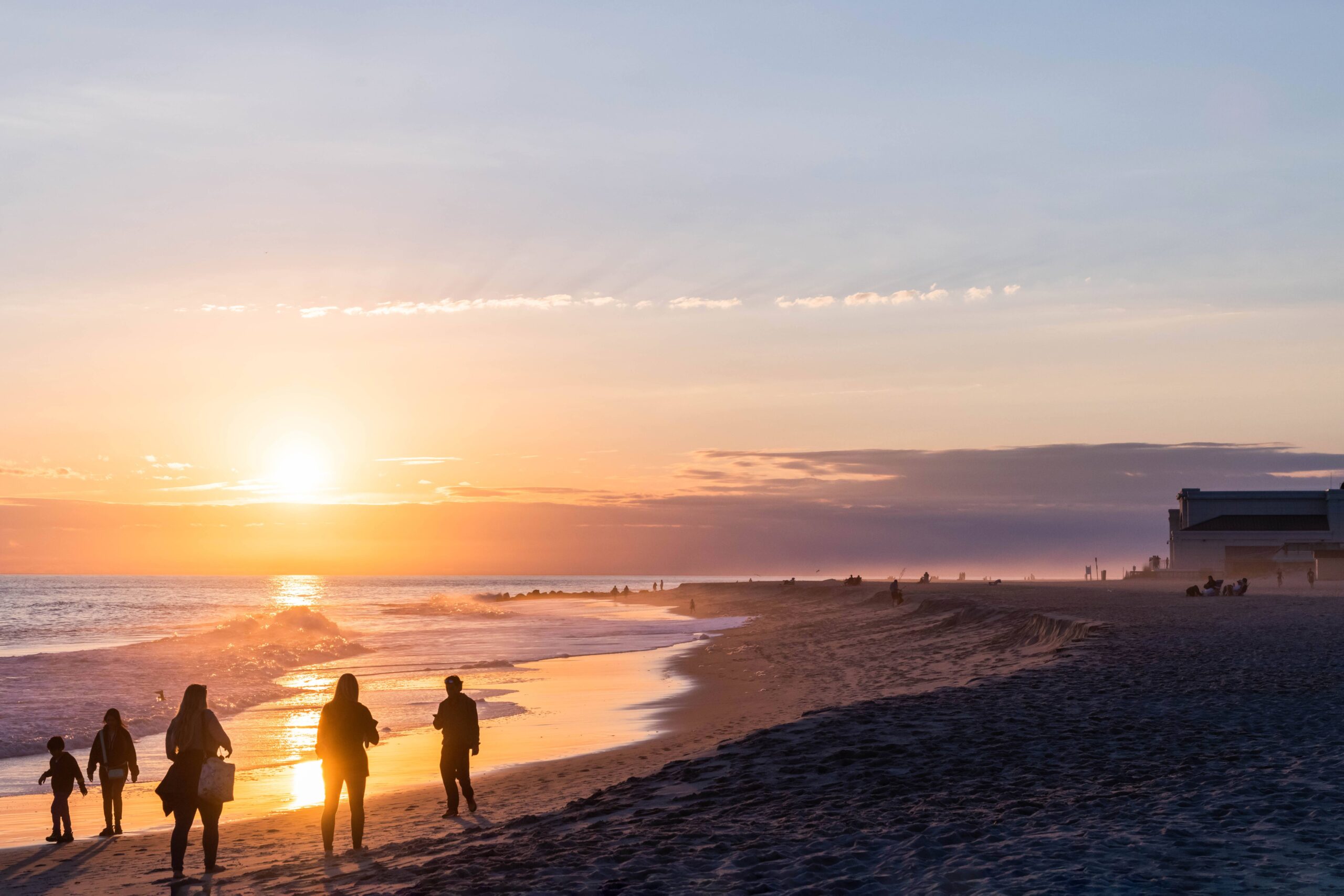 People walking along the ocean at sunset. One cloud is at the horizon, and mist is coming off the ocean