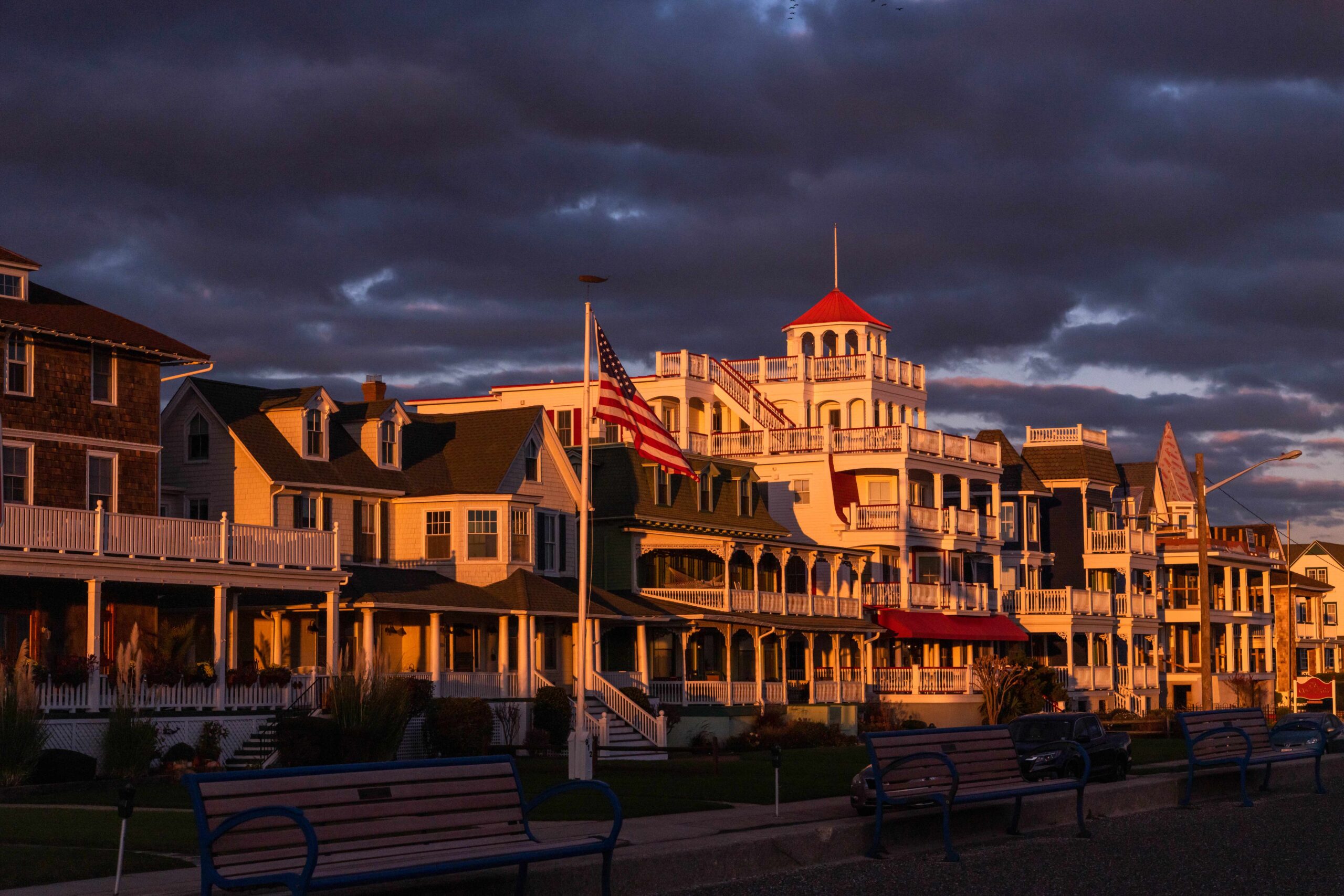 Sunset light shining on Victorian houses on Beach Ave with purple clouds in the sky and the promenade benches in the foreground