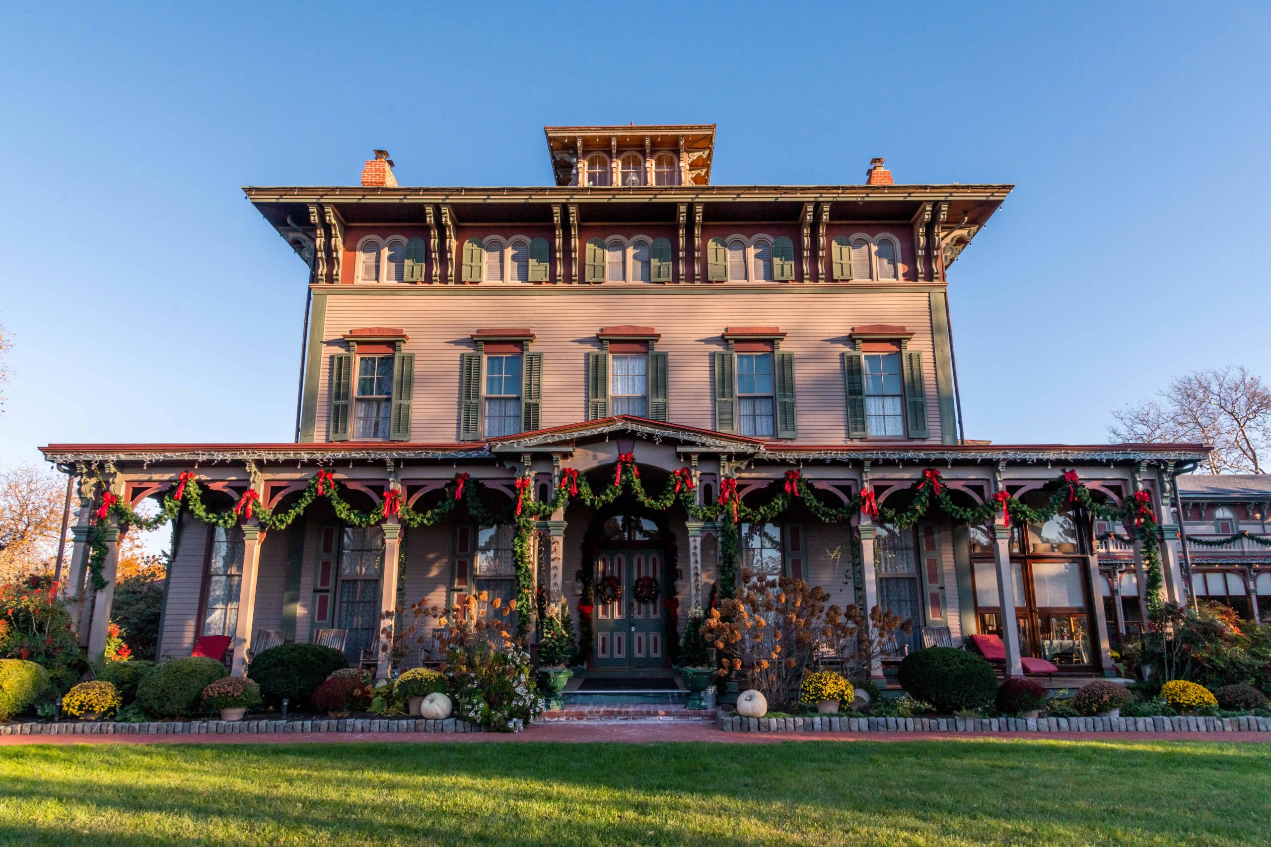 The front of the Southern Mansion, a Victorian bed and breakfast, decorated with green garland and red bows on a sunny day with a clear blue sky