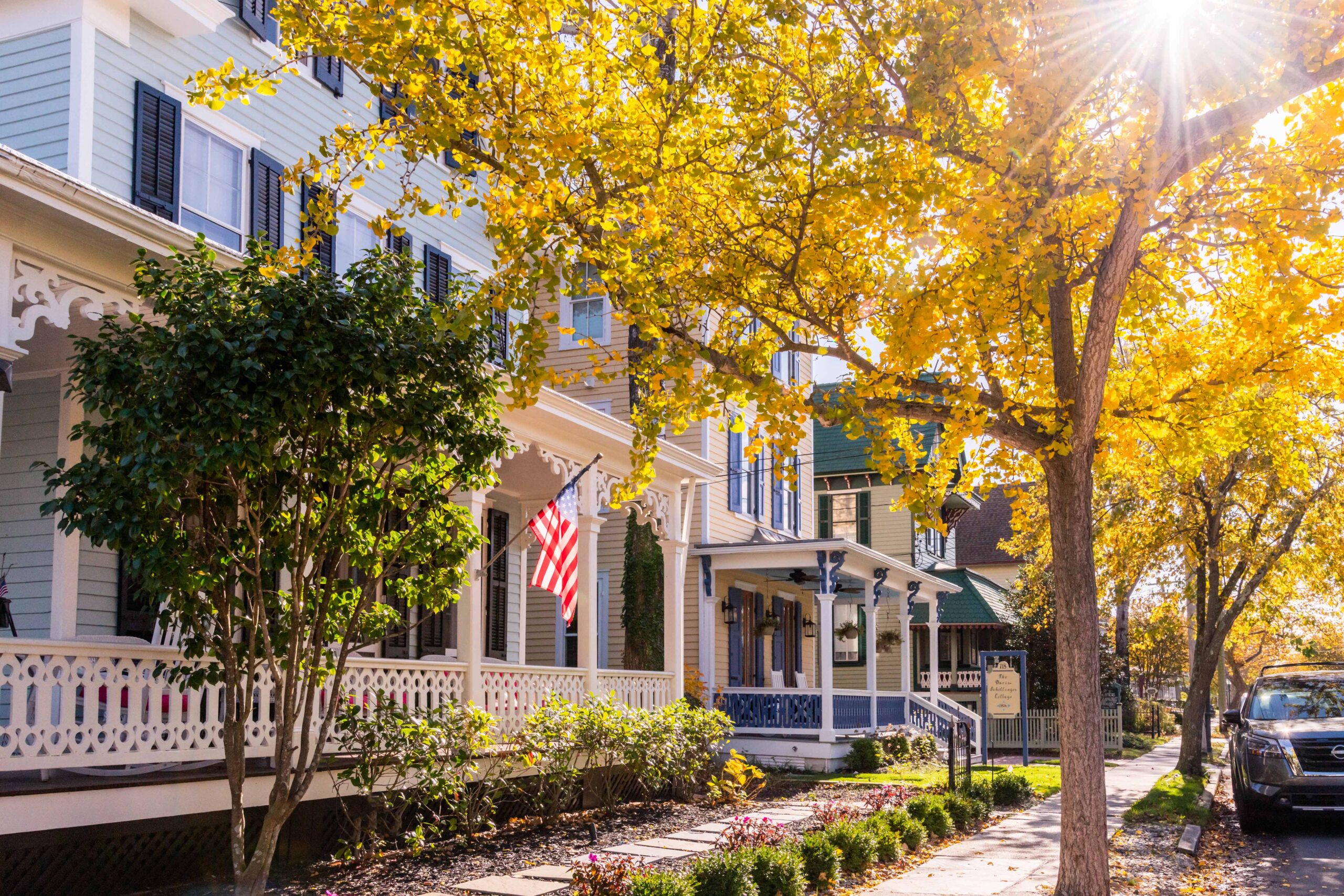 Sunlight shining through tree with yellow leaves on a sidewalk with Victorian styled houses and front porches