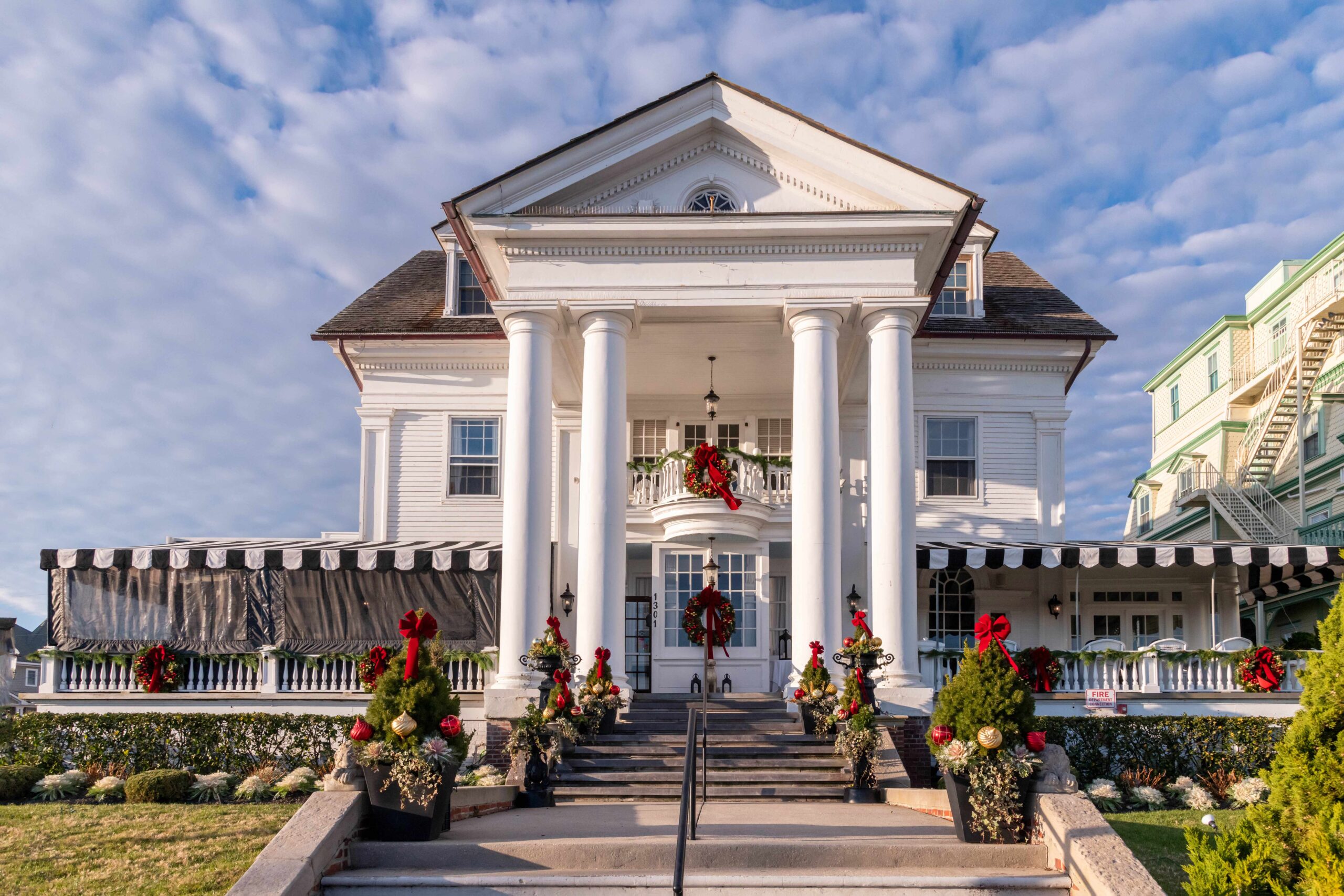 The front of Peter Shields Inn, a Victorian bed and breakfast, decorated with wreaths, evergreen, and red bows on a sunny afternoon with thin white clouds in a blue sky