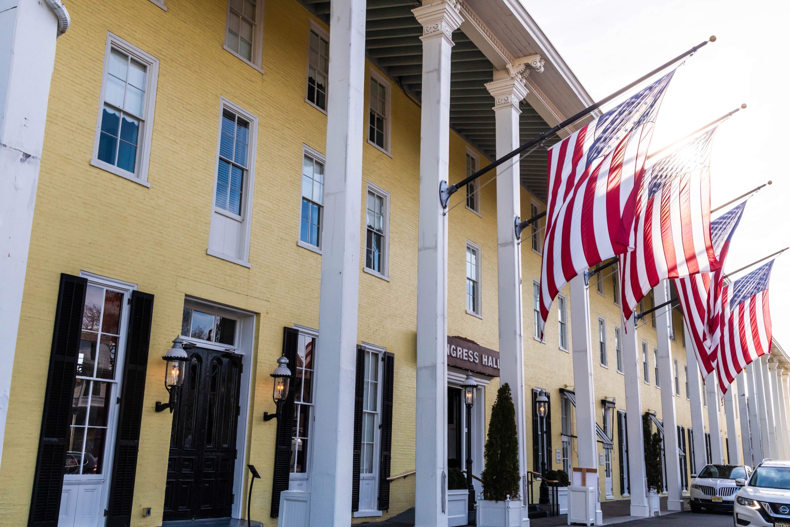 Sunshine streaming through American Flags hanging at Congress Hall, a yellow Victorian style hotel