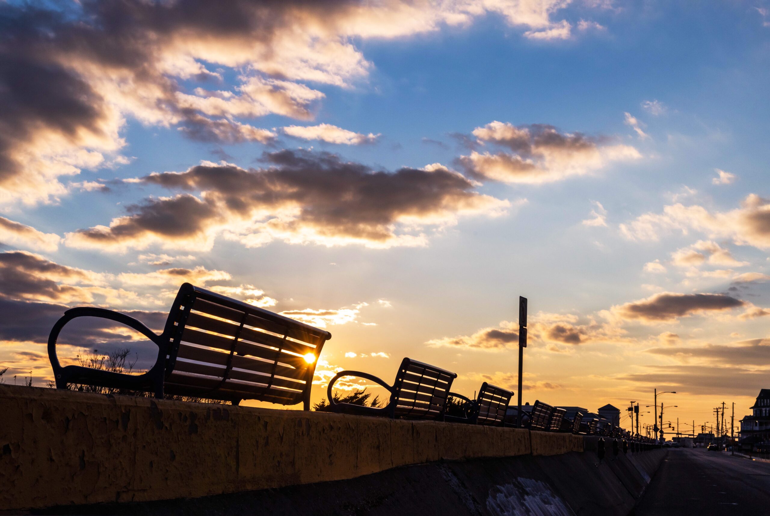 Sun setting behind a bench on the promenade with some puffy clouds in the sky
