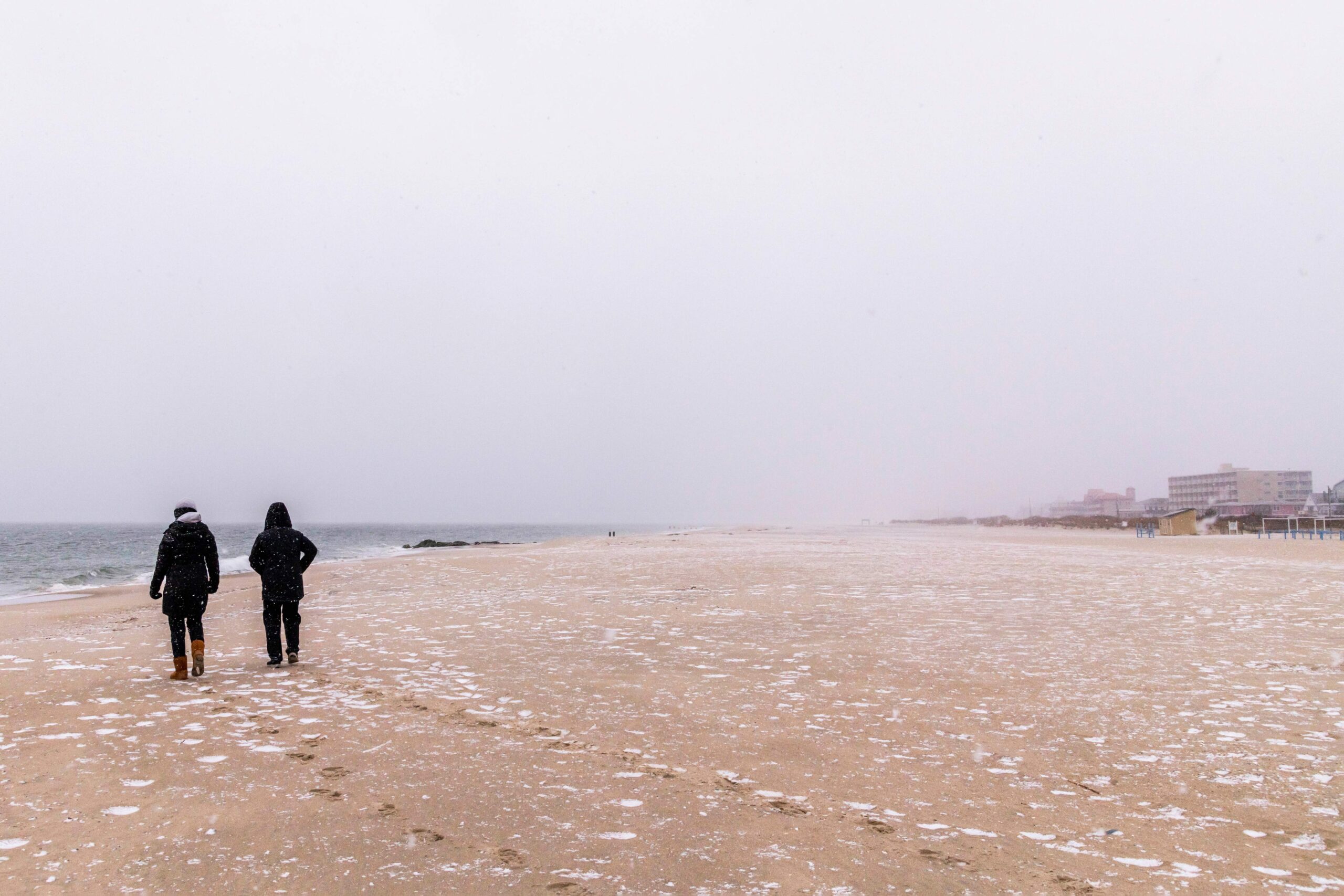 Two people walking on the beach with a cloudy sky and snow in the sand