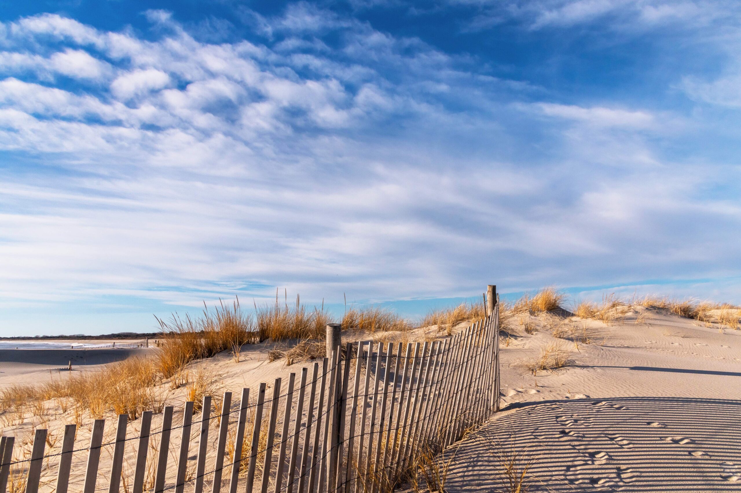 The dunes and fence at the beach with white wispy clouds in a blue sky