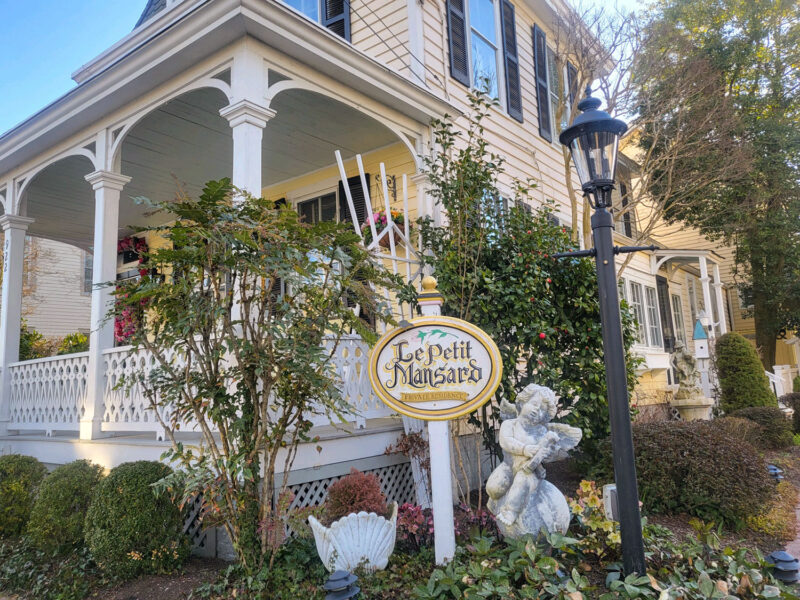 Garden and porch of Le Petit Mansard, a yellow and white Victorian house