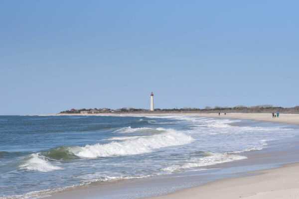 A Day at The Cove with people walking the beach with the Cape May Lighthouse off in the distance.