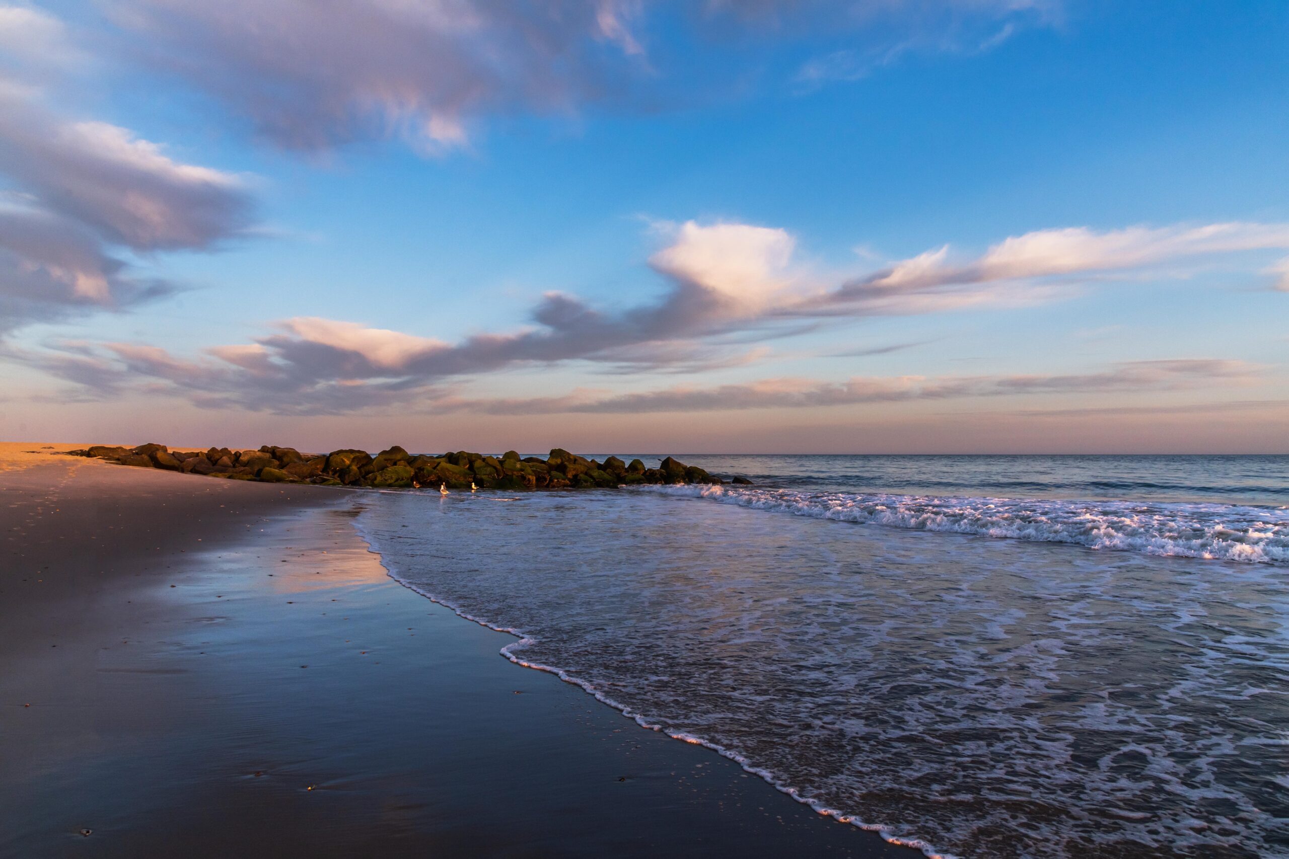 Wispy clouds in a blue and pink sky reflected in the ocean and the shoreline at the beach