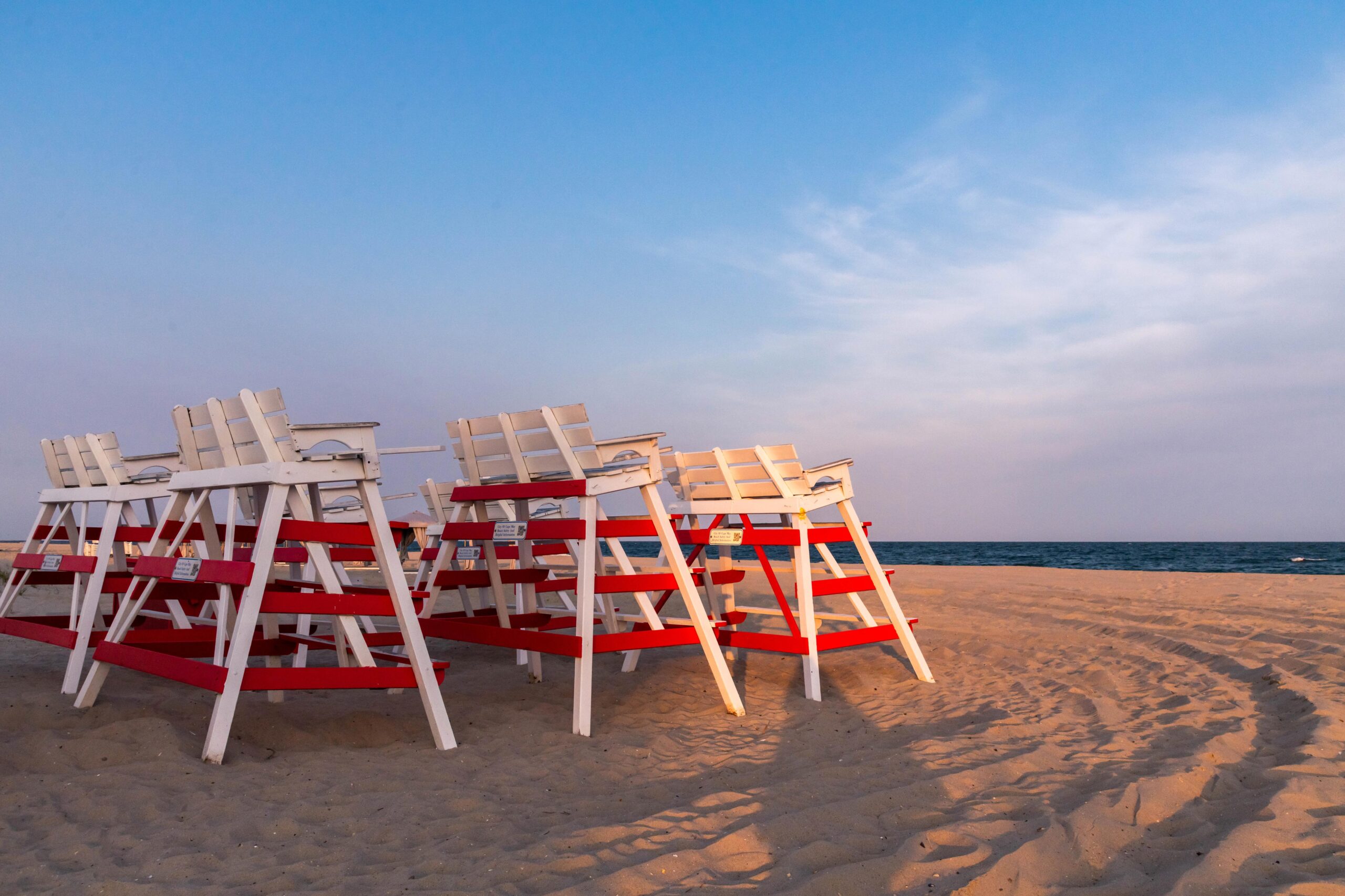 A group of lifeguard stands on the beach at sunset with a blue sky and wispy pink clouds